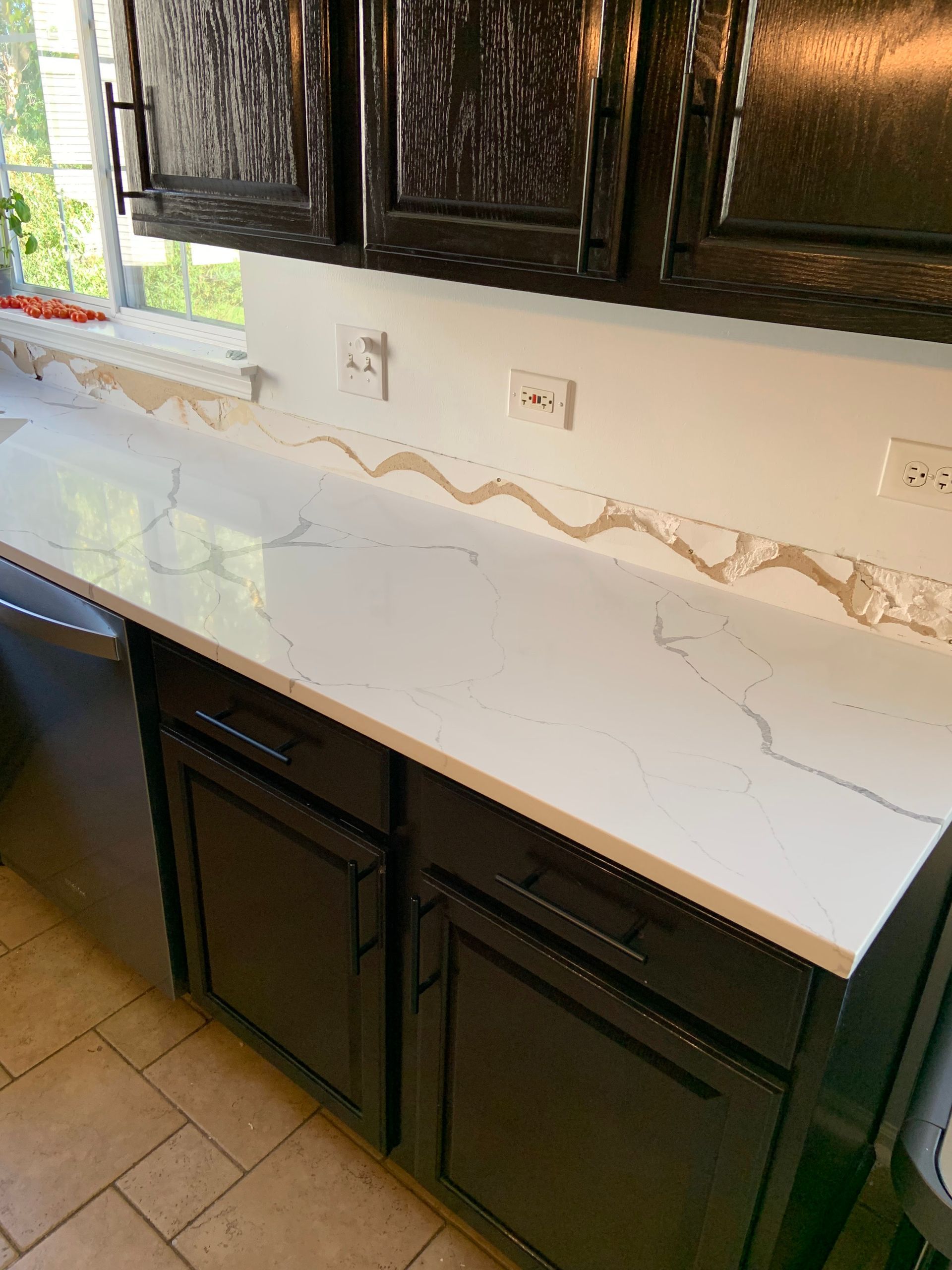 White quartz kitchen countertop with dark cabinets and upper cupboards beneath a window