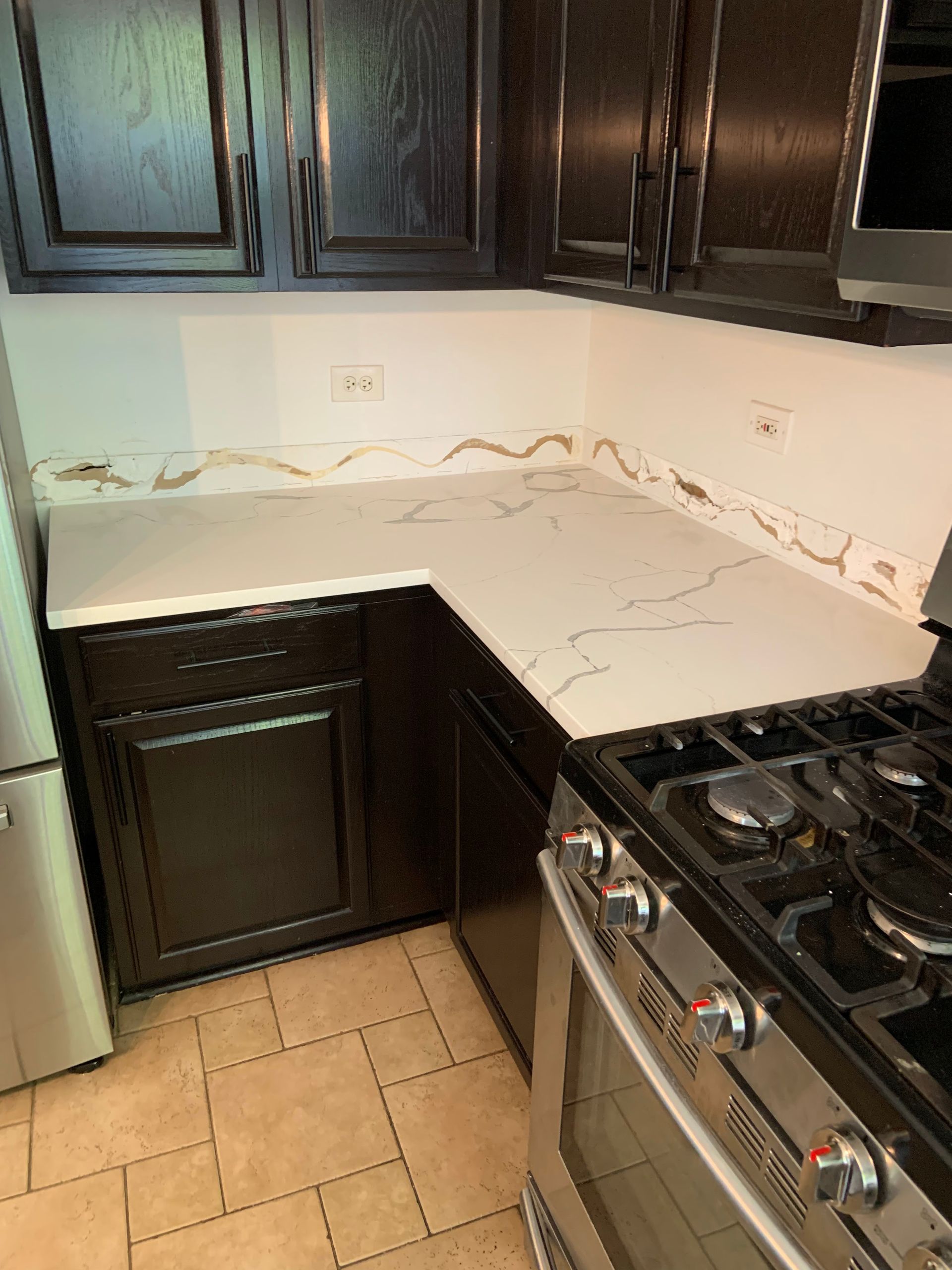 Kitchen corner with dark cabinets, white countertops, tiled floor, and stainless gas stove.