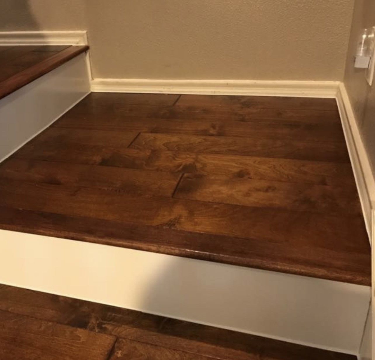 Wooden stair landing with dark stain, white trim, and beige walls indoors