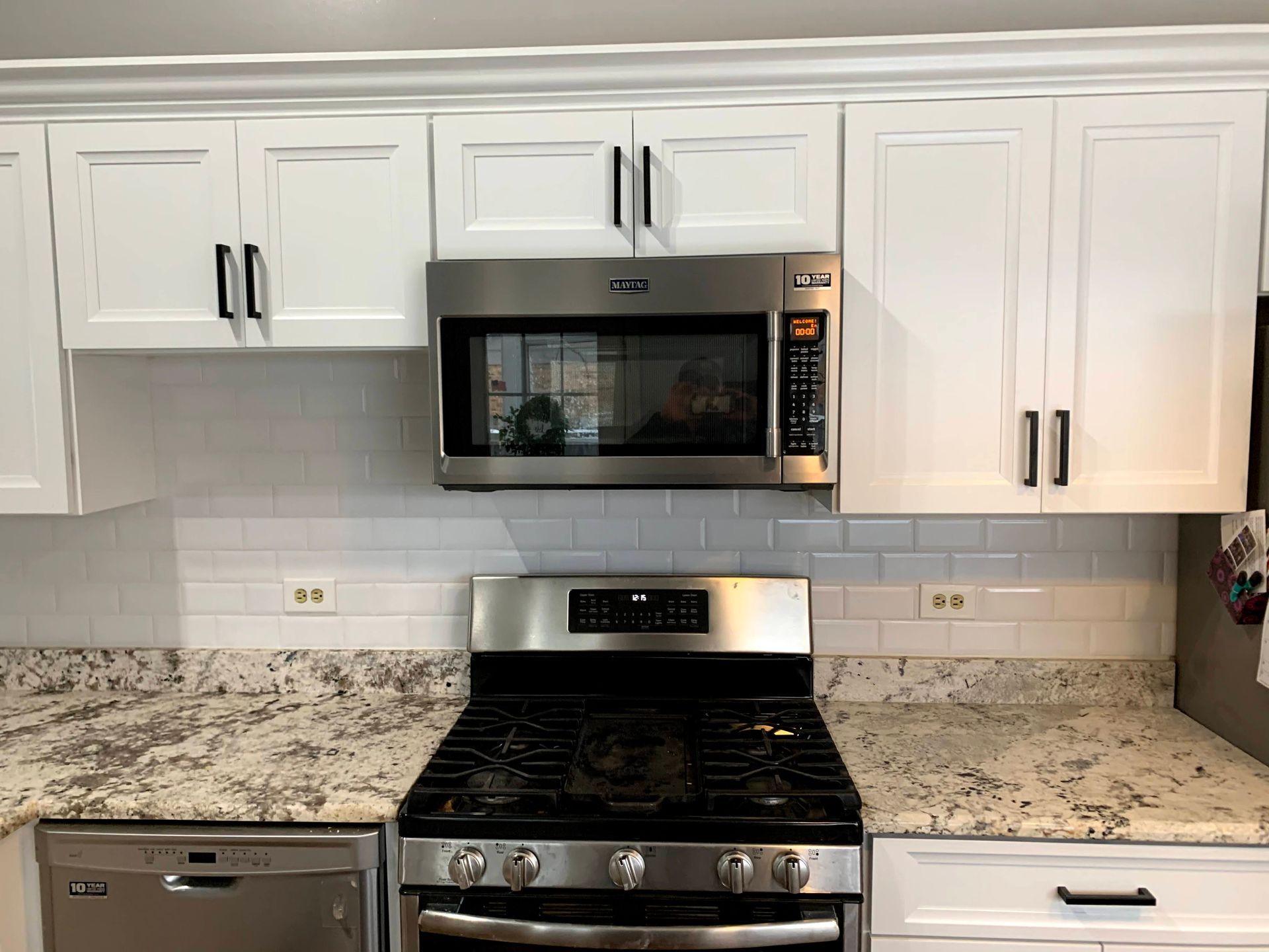 Modern kitchen with white cabinets, stainless steel stove and microwave, and speckled granite countertops