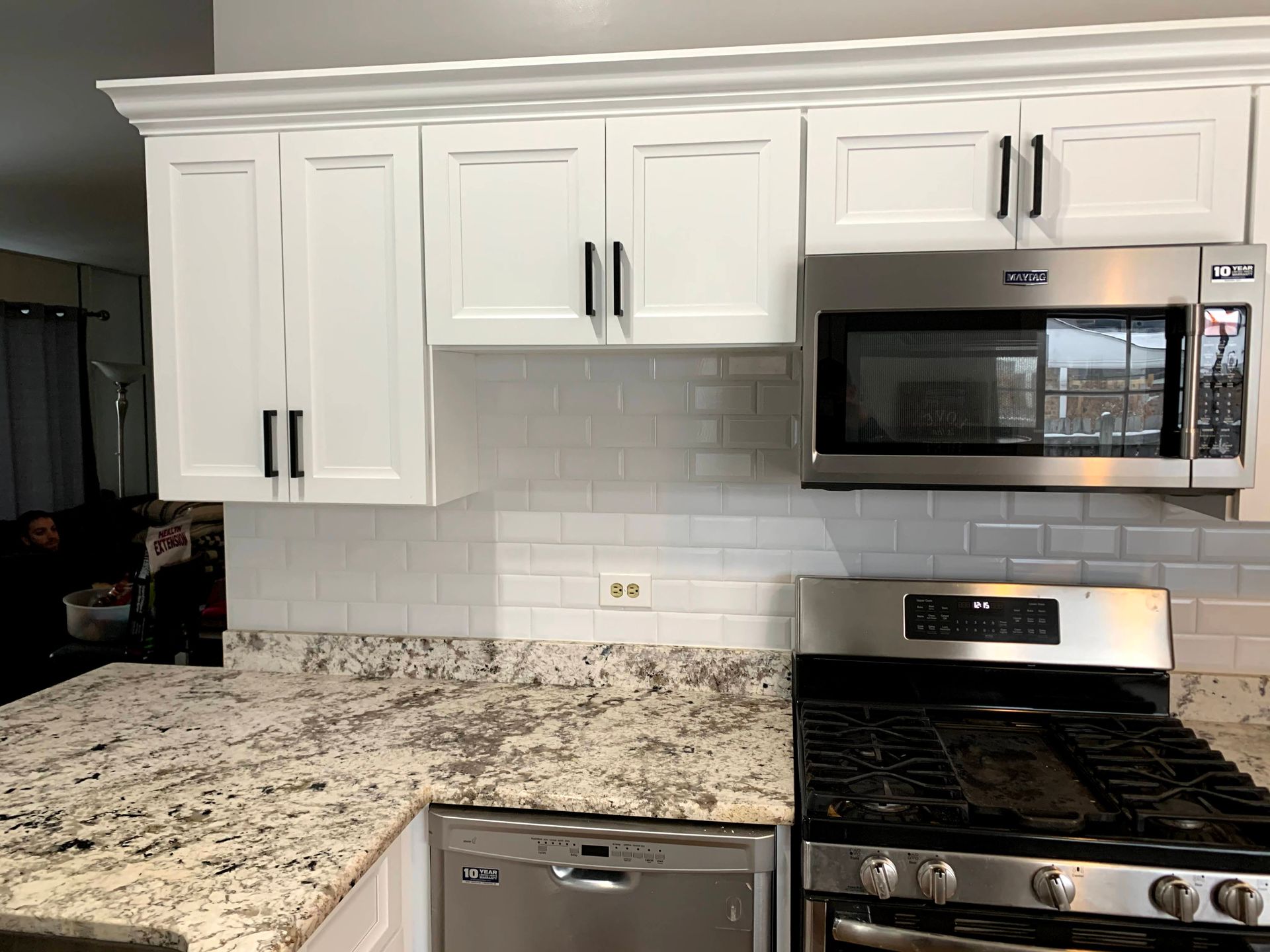 White kitchen with granite countertops, subway tile backsplash, white cabinets, and stainless steel microwave and stove.