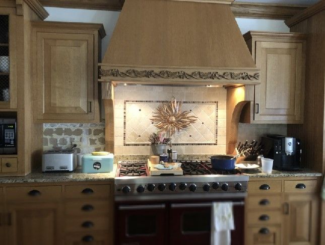 Wooden kitchen with stovetop under a decorative range hood, framed by light cabinets and countertop appliances