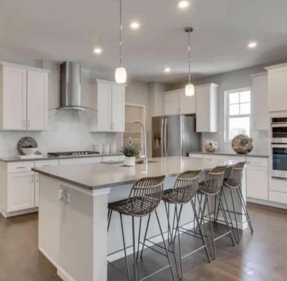 Modern white kitchen with island, pendant lights, stainless steel appliances, and four bar stools