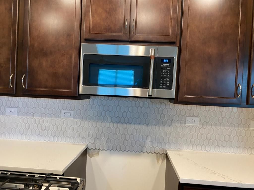 Kitchen with dark wood cabinets, stainless steel microwave, and light countertop backsplash.