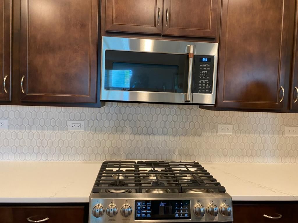 Modern kitchen with dark wood cabinets, stainless steel microwave, and gas range under tiled backsplash.