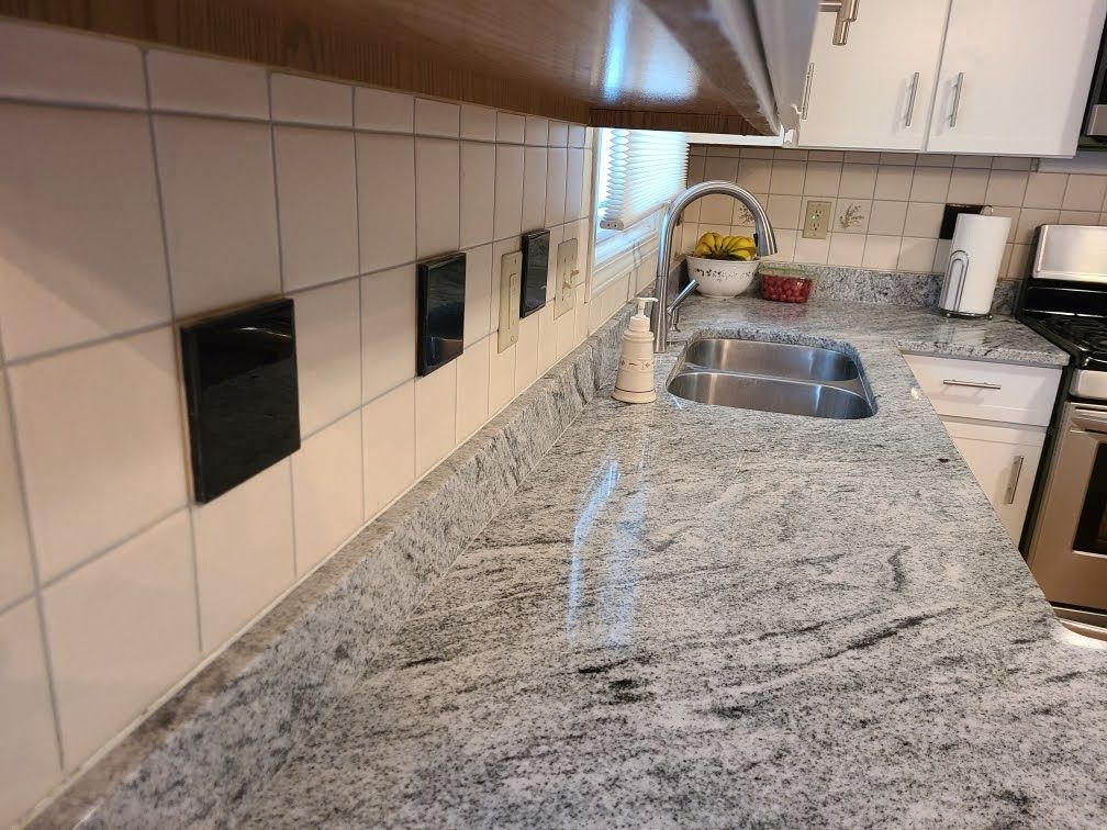 Kitchen countertop with gray granite, white tile backsplash, and double sink near a window.