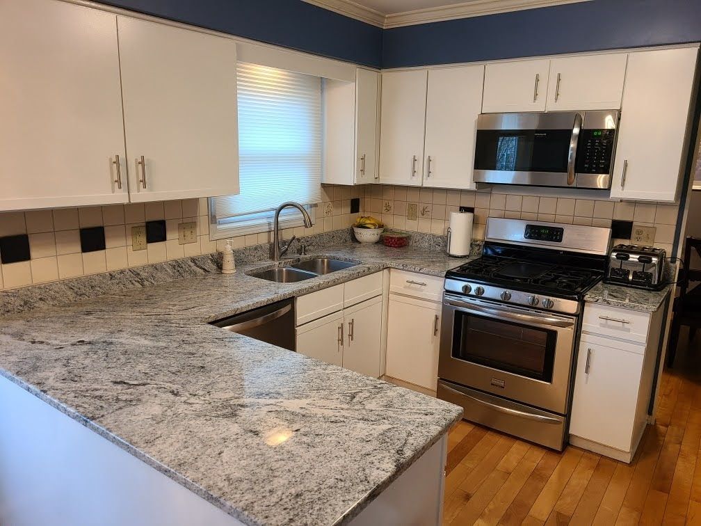 Bright kitchen with white cabinets, granite countertops, stainless steel stove, and a window over the sink.