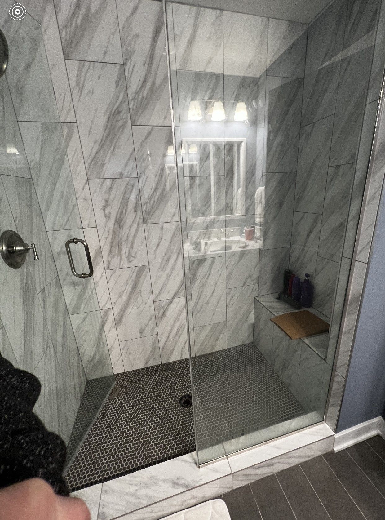 Modern tiled shower with glass door, bench, window, and dark pebble floor mat