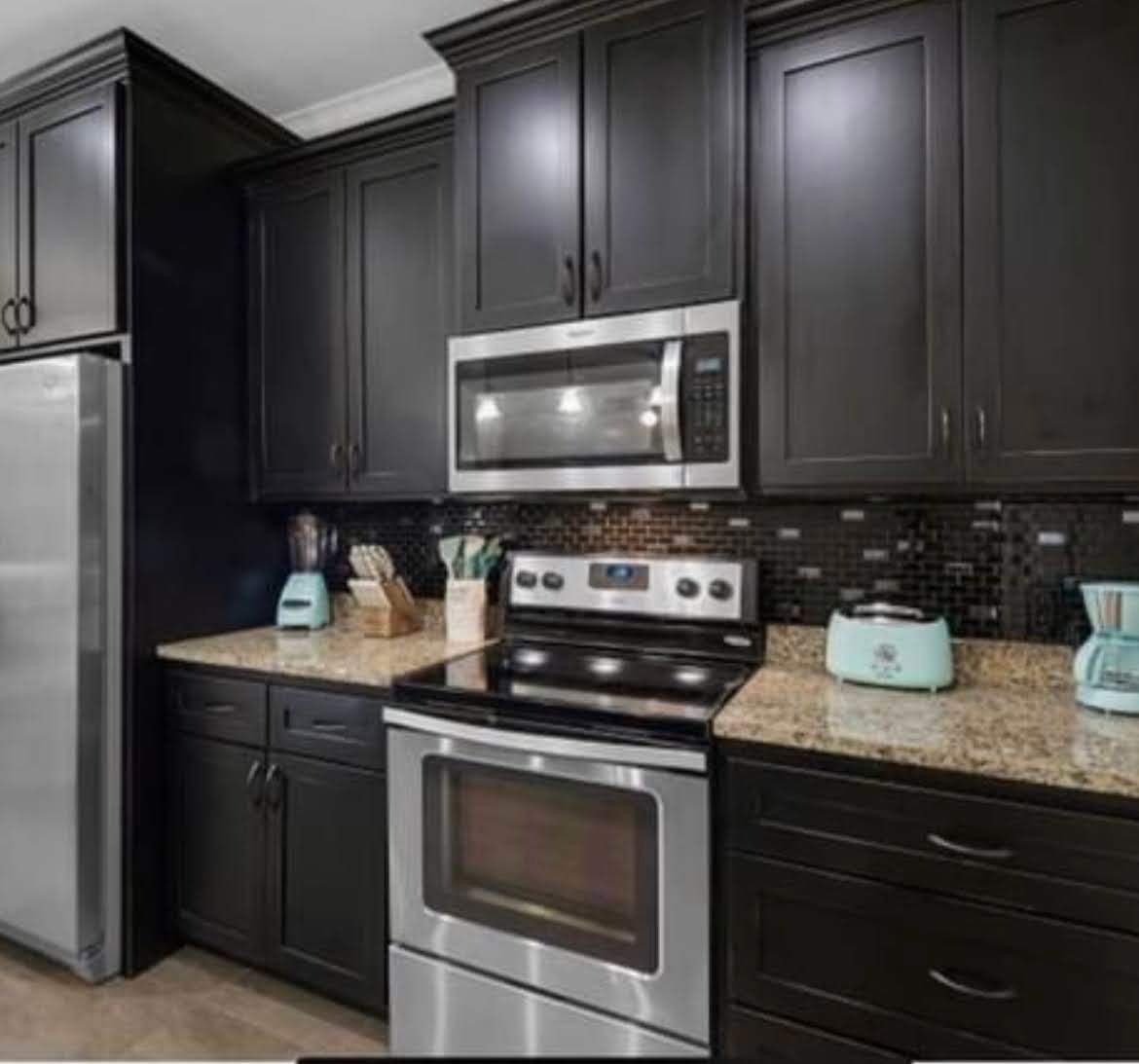 Modern kitchen with dark cabinets, stainless steel appliances, granite countertop, and mosaic tile backsplash