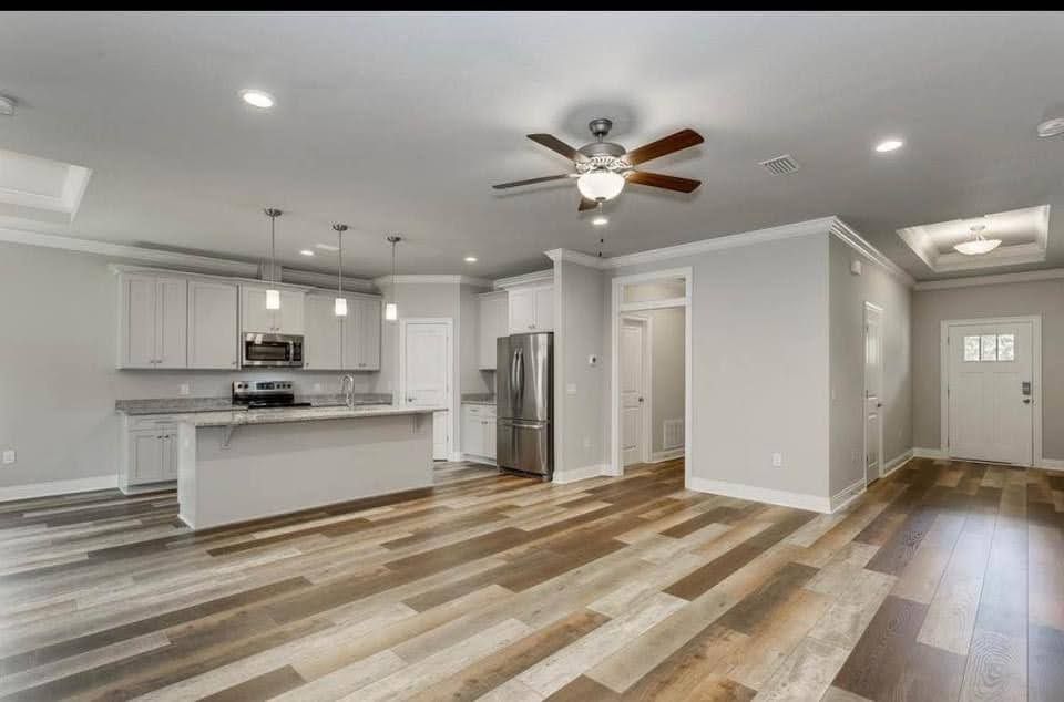 Spacious modern kitchen and living area with white cabinets, gray walls, wood floors, and ceiling fan