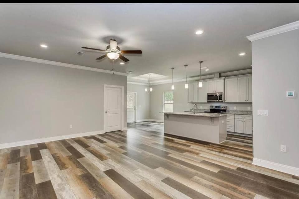 Open-concept living room and kitchen with gray walls, wood-pattern floors, and ceiling fan lights.