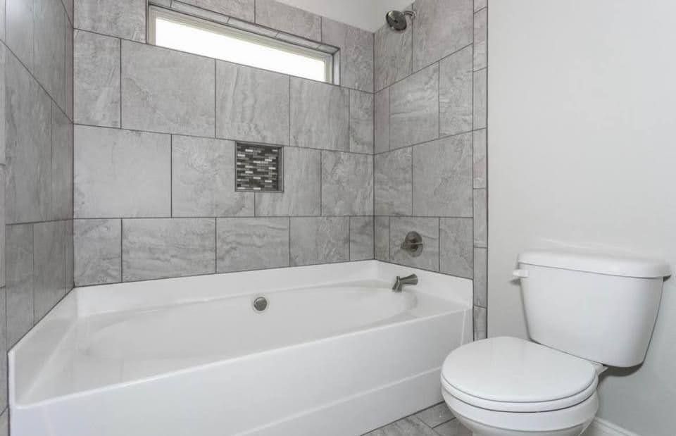 Modern bathroom with white tub, gray tiled shower walls, and a toilet
