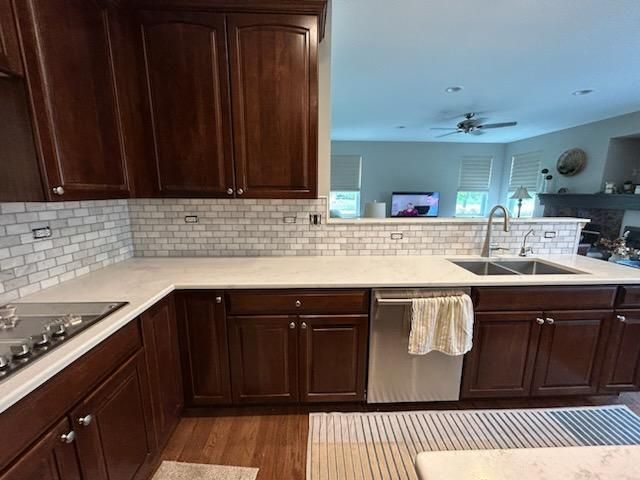 Kitchen with dark wood cabinets, light tile backsplash, granite countertop, and stainless-steel sink and stove