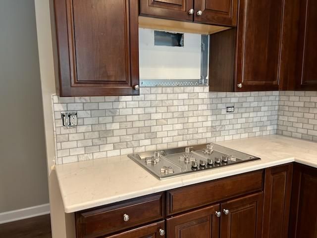 Kitchen with dark wood cabinets, white subway tile backsplash, and a stainless steel stove beneath a vent hood.