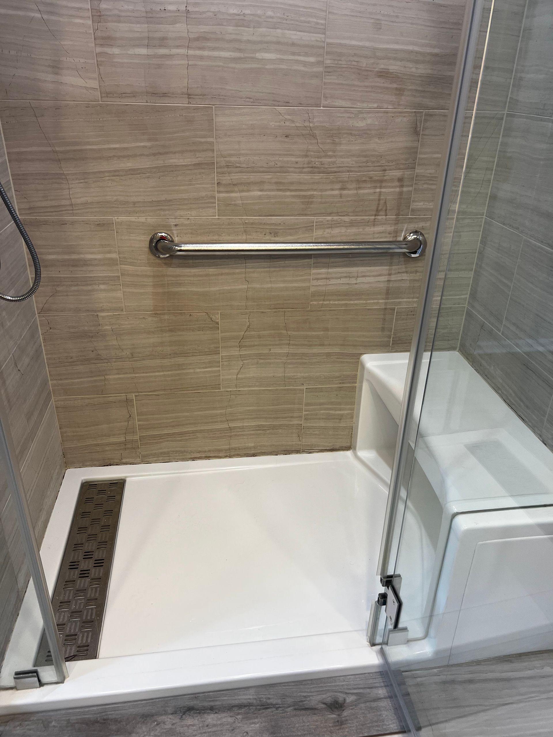 Accessible shower with grab bar, glass door, and white shower floor in a tiled bathroom