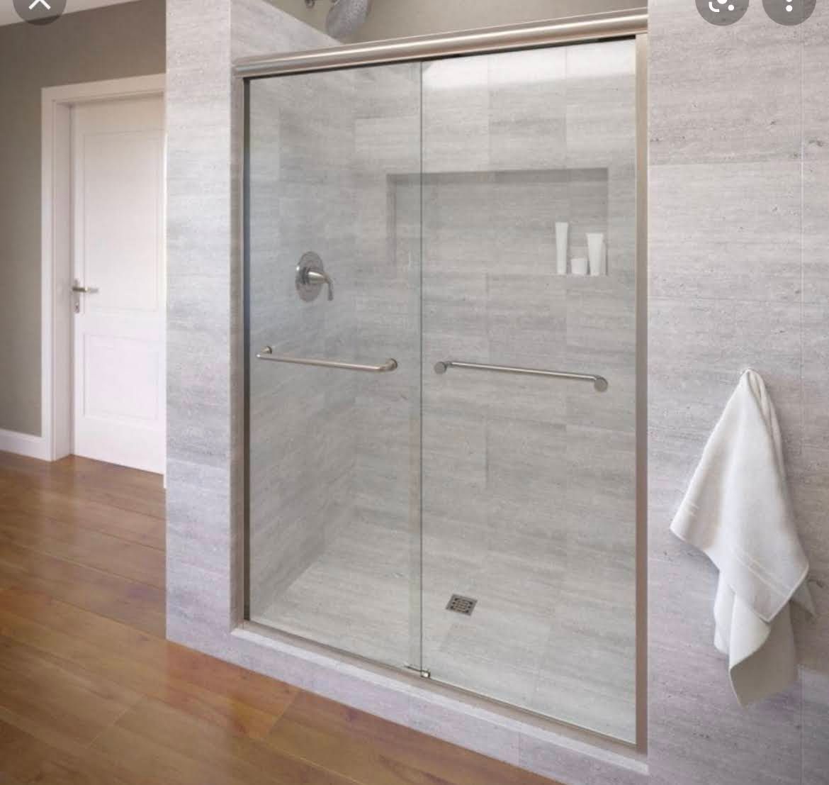 Modern walk-in shower with clear glass doors, gray tile, and a white towel hanging on the wall.