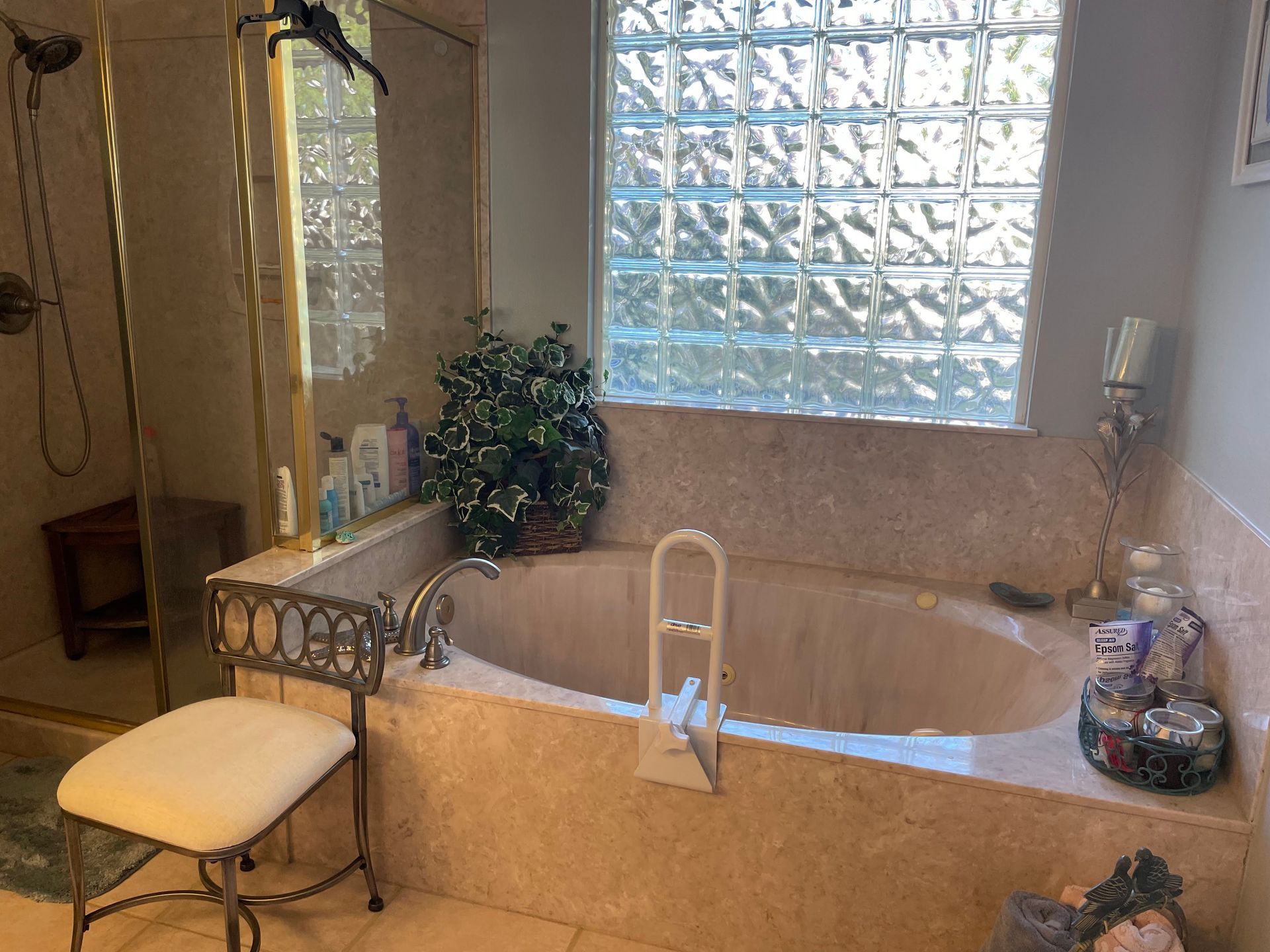 Bathroom with a corner soaking tub, cream tile, frosted glass block window, and a cushioned stool beside it
