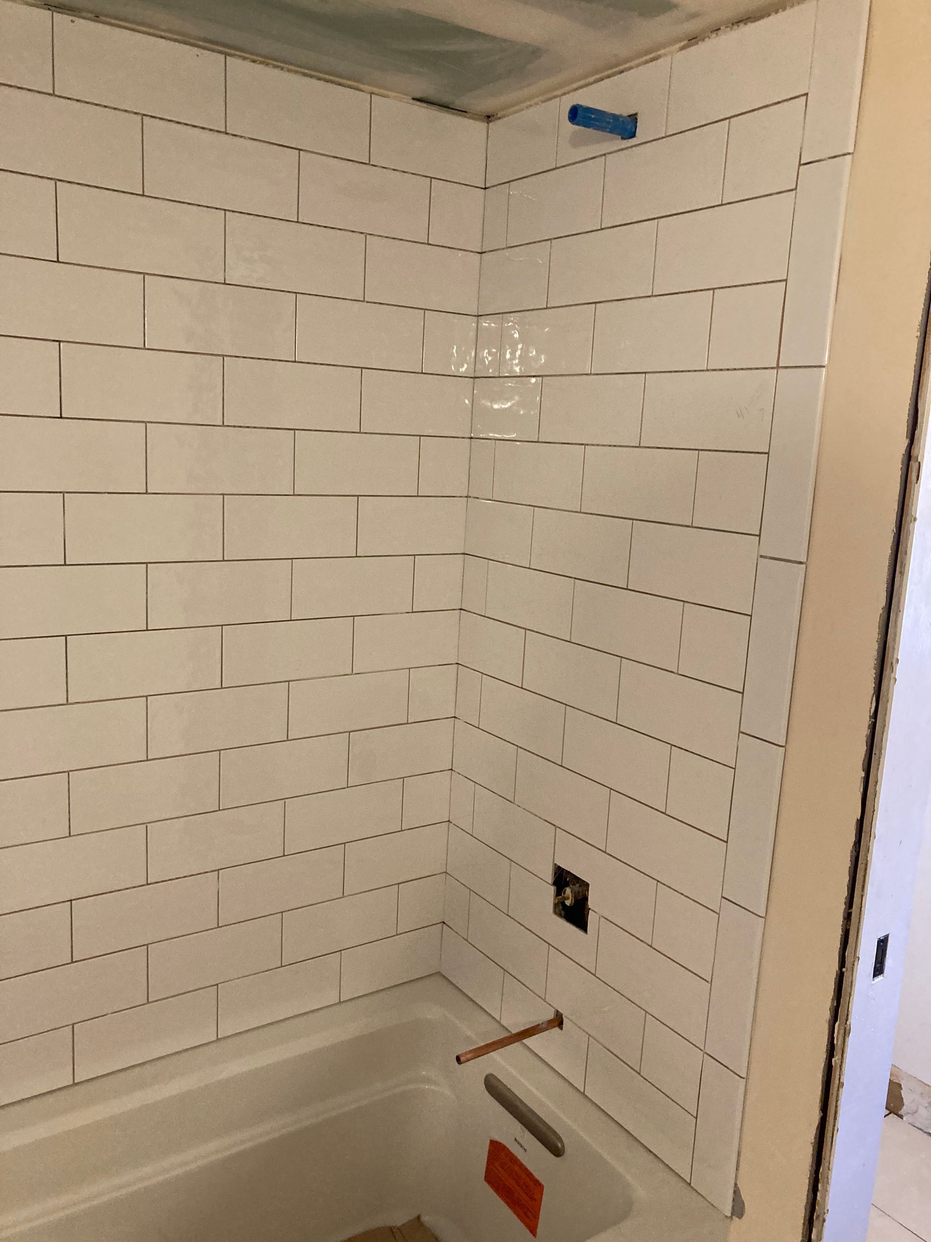 Partially tiled bathtub/shower alcove with white subway tile and exposed fixtures under renovation