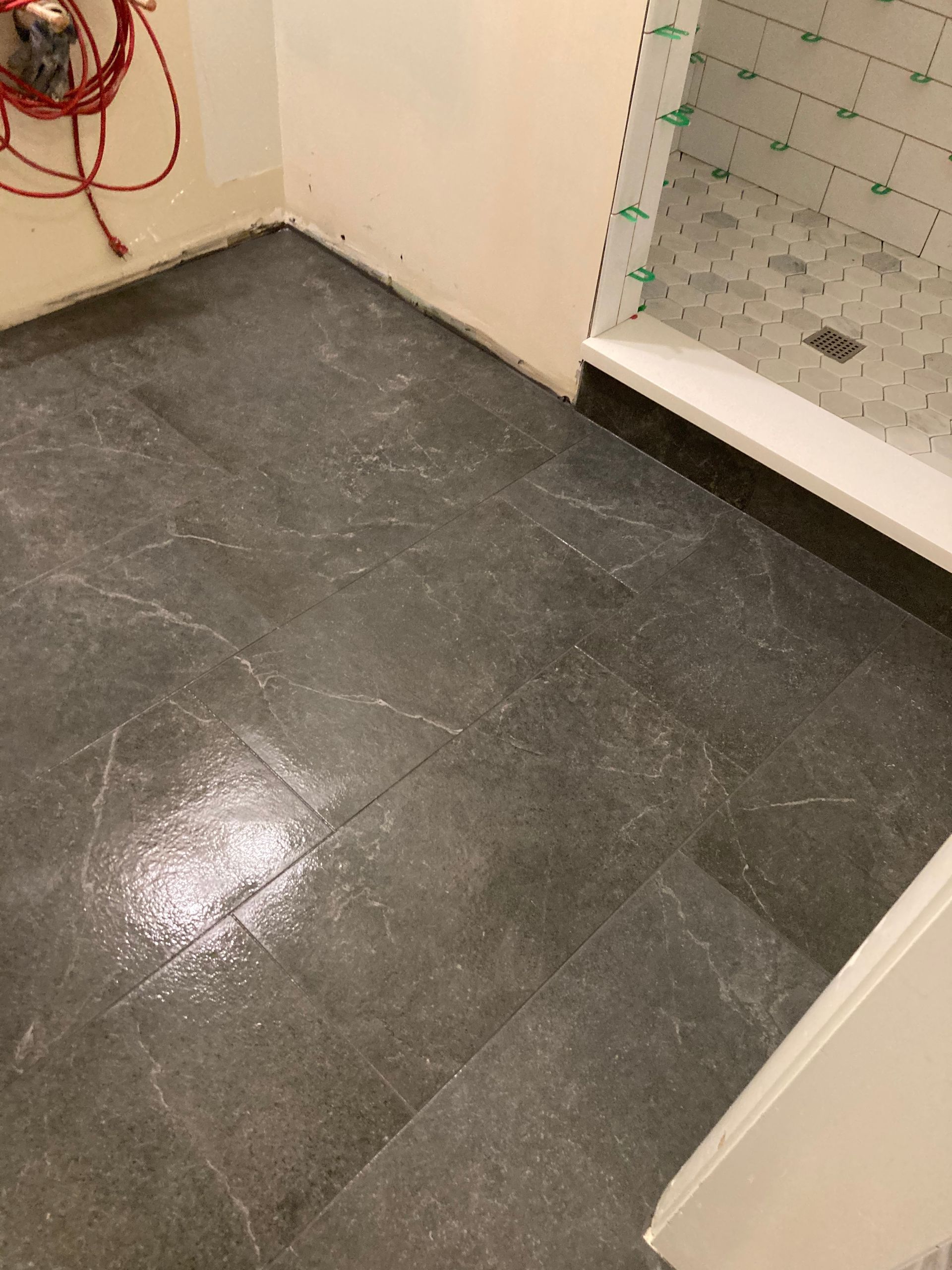 Empty bathroom floor with dark gray tile and a tiled shower area on the right.