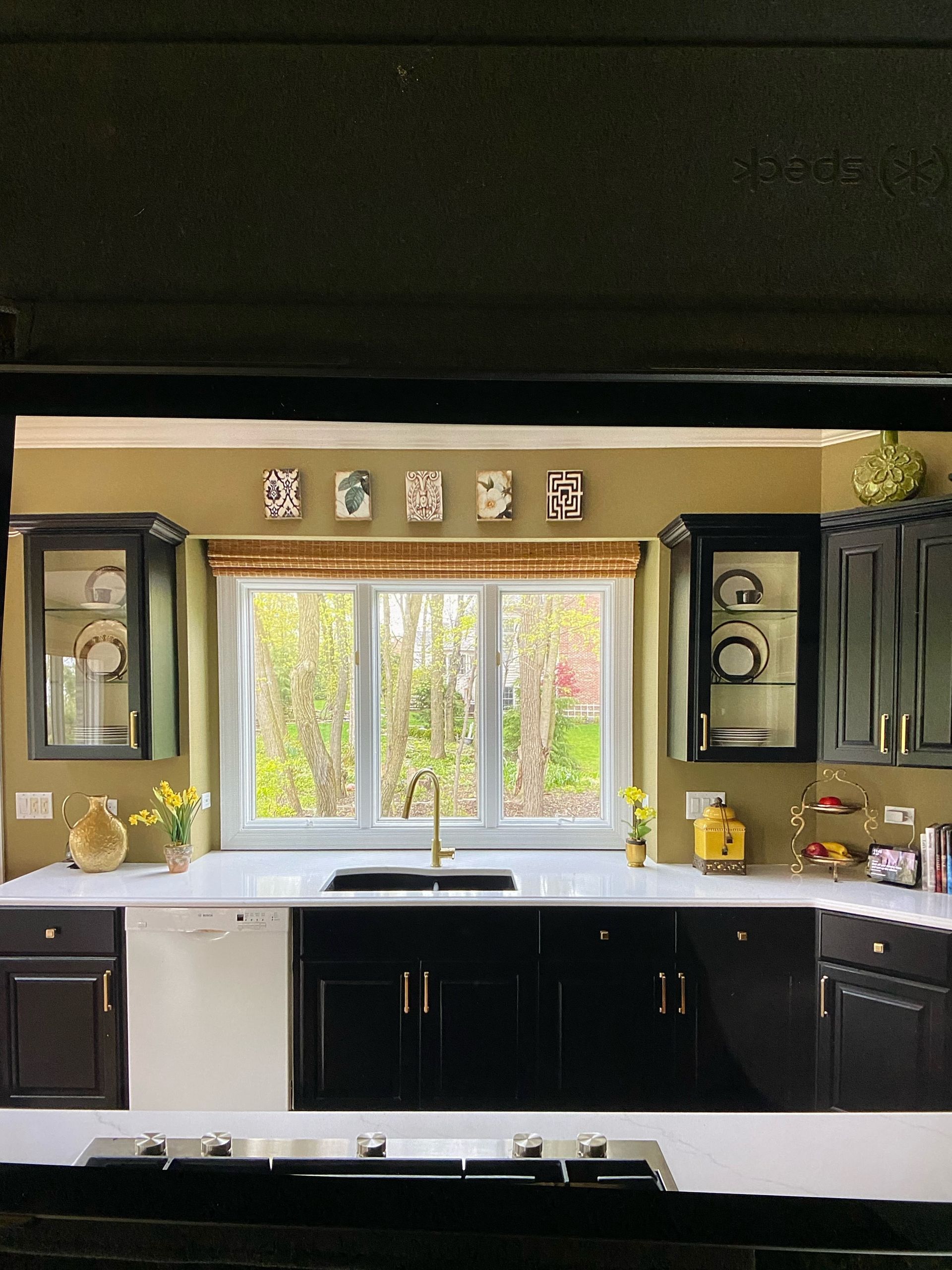 Modern kitchen with black cabinets, white sink, and bright window centered above the counter.