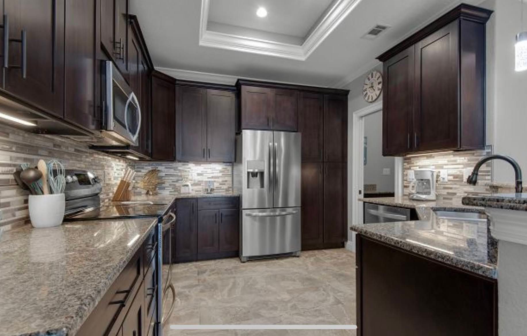 Modern kitchen with dark wood cabinets, stainless steel refrigerator, granite counters, and recessed lighting