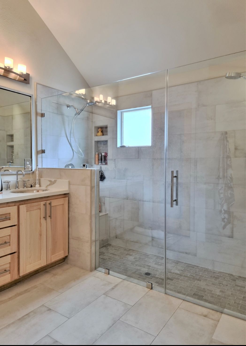 Modern bathroom with glass shower enclosure, marble tile, and light wood vanity