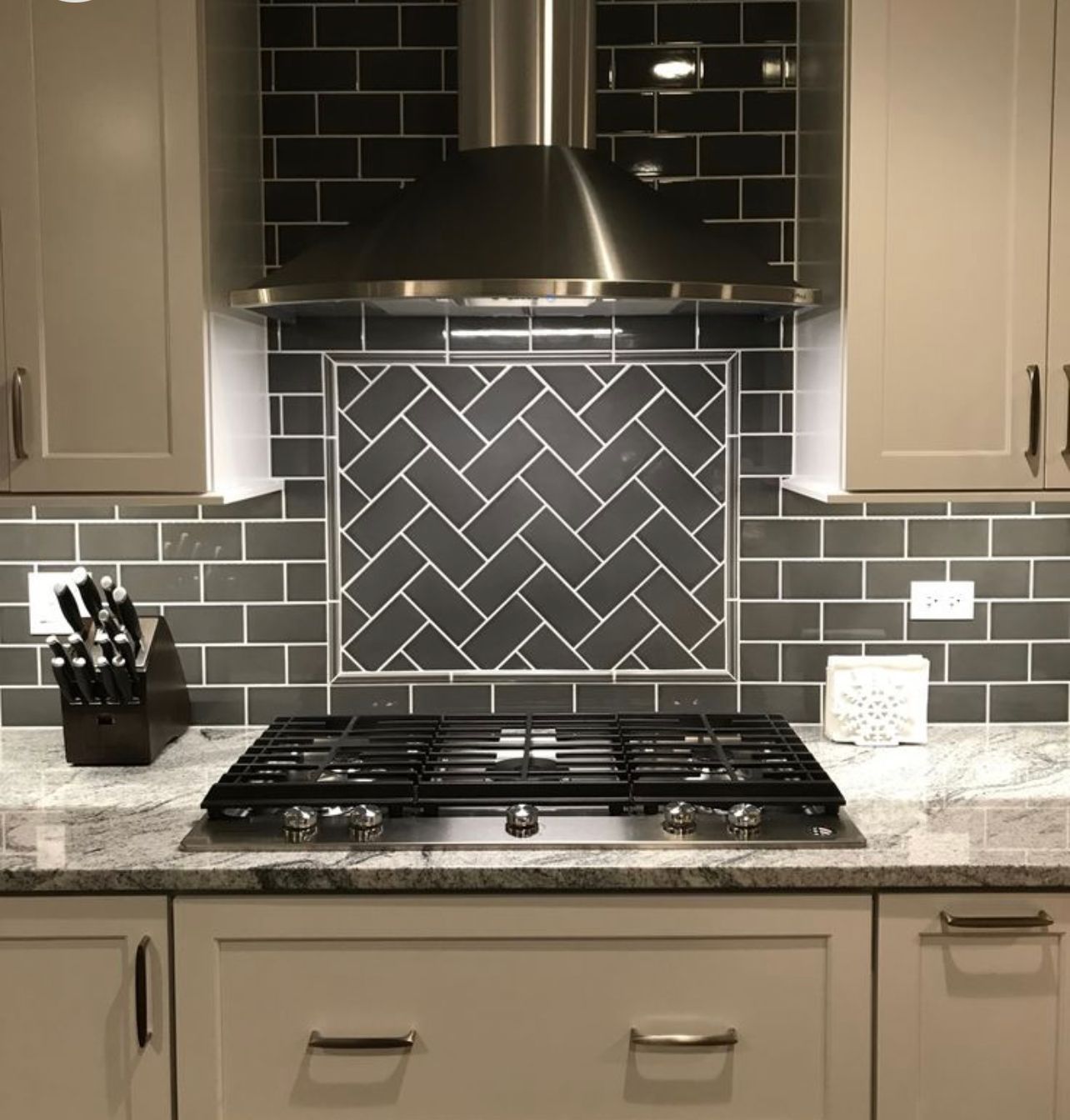 Modern kitchen backsplash with black range hood, gas cooktop, and gray tile walls