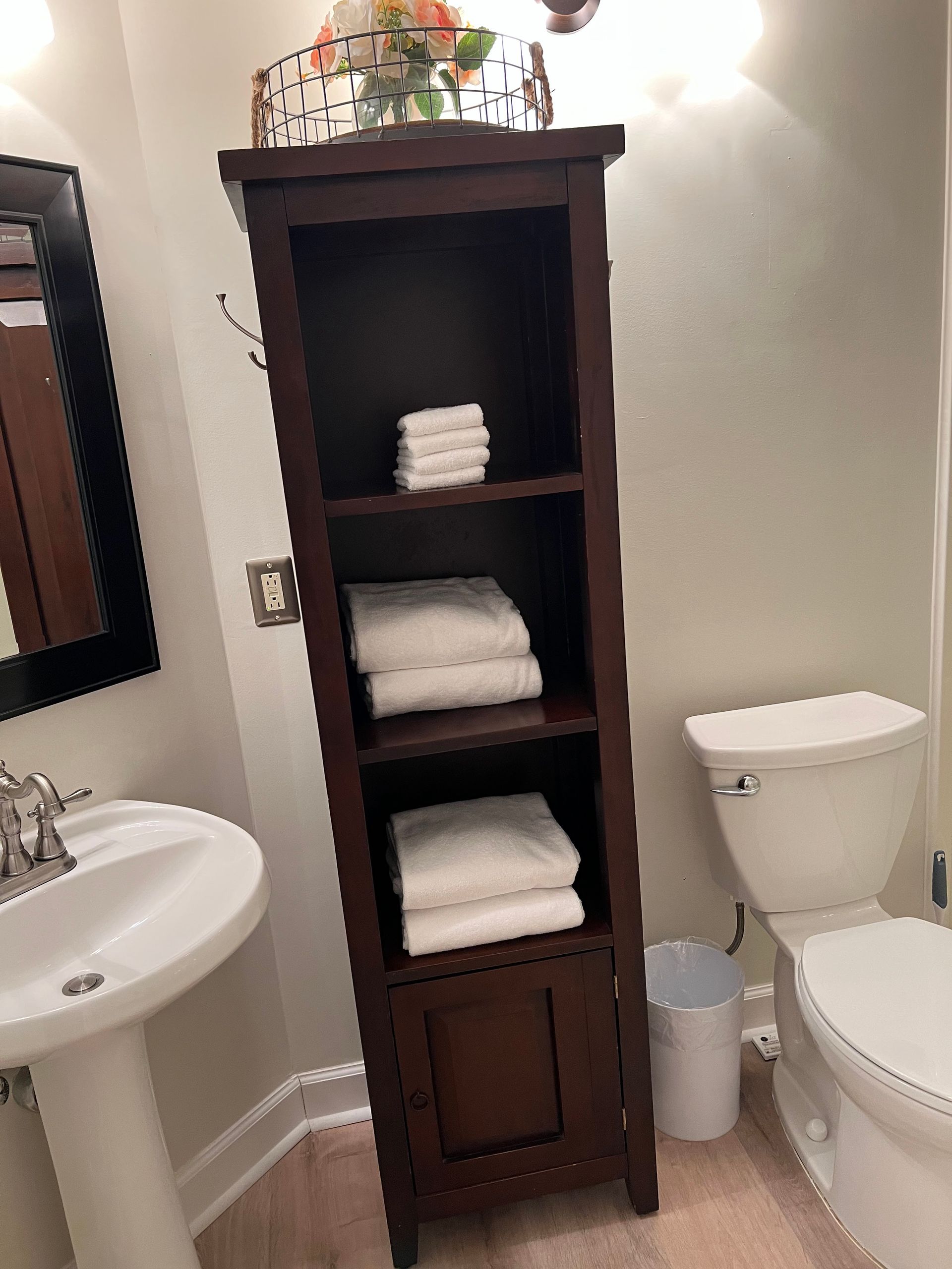 Small bathroom with a dark wood towel cabinet, pedestal sink, toilet, and white towels.