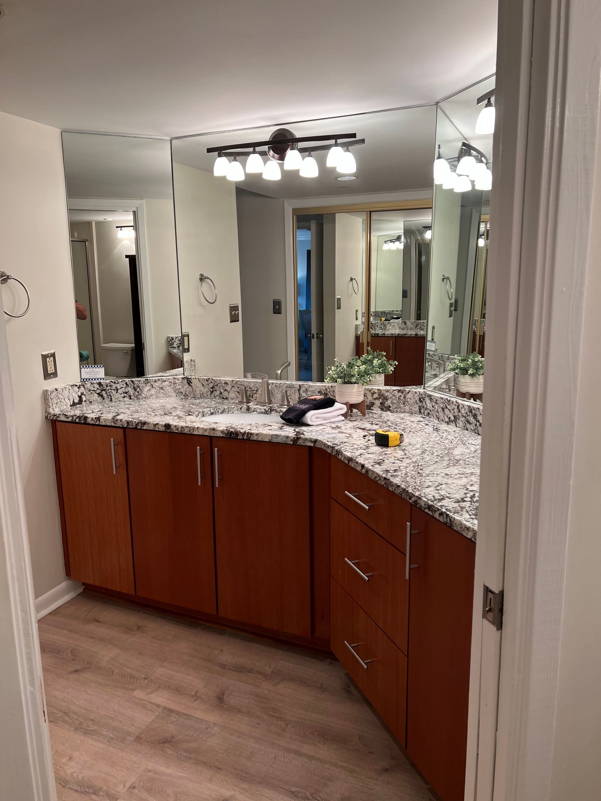 Bathroom vanity with granite countertop, wood cabinets, and mirror under bright lights