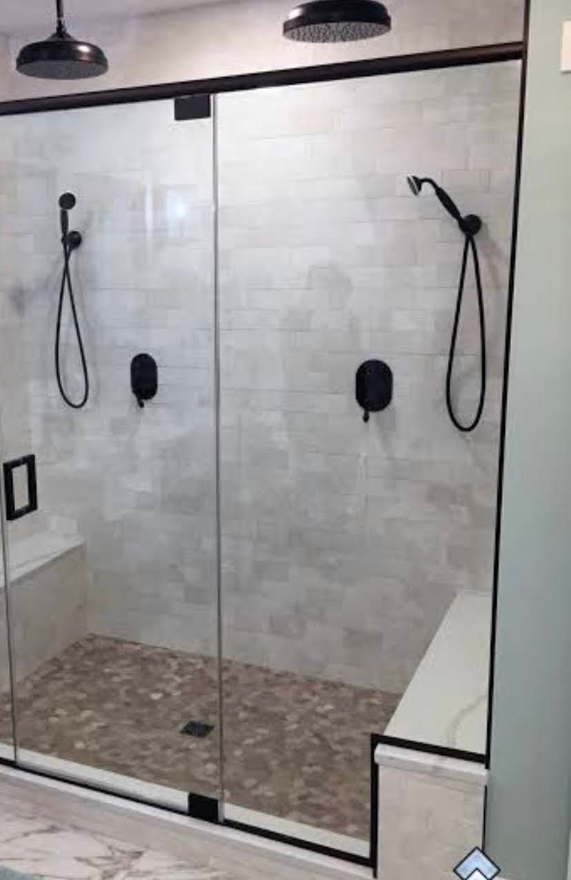 Modern walk-in shower with glass doors, beige tile walls, and two black showerheads.