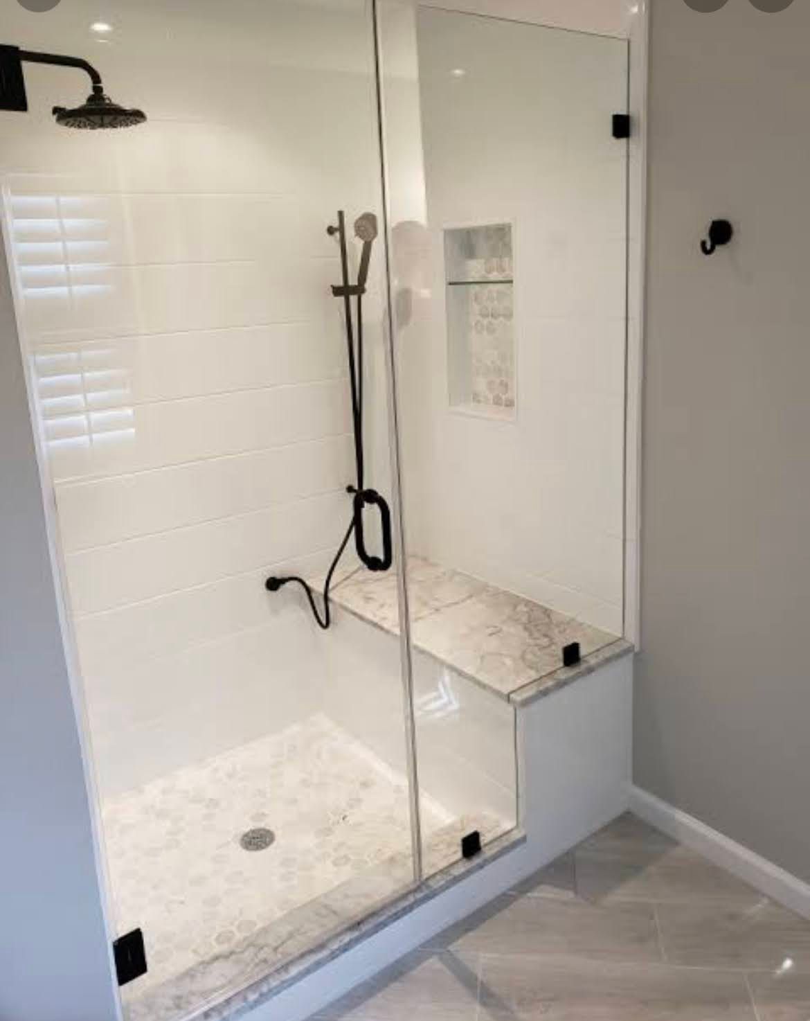 Modern glass shower enclosure with white tile walls and built-in bench in a bathroom