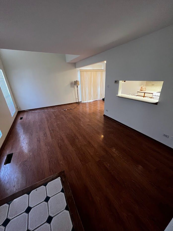 Empty living room with dark wood floors, white walls, and a pass-through window to the kitchen