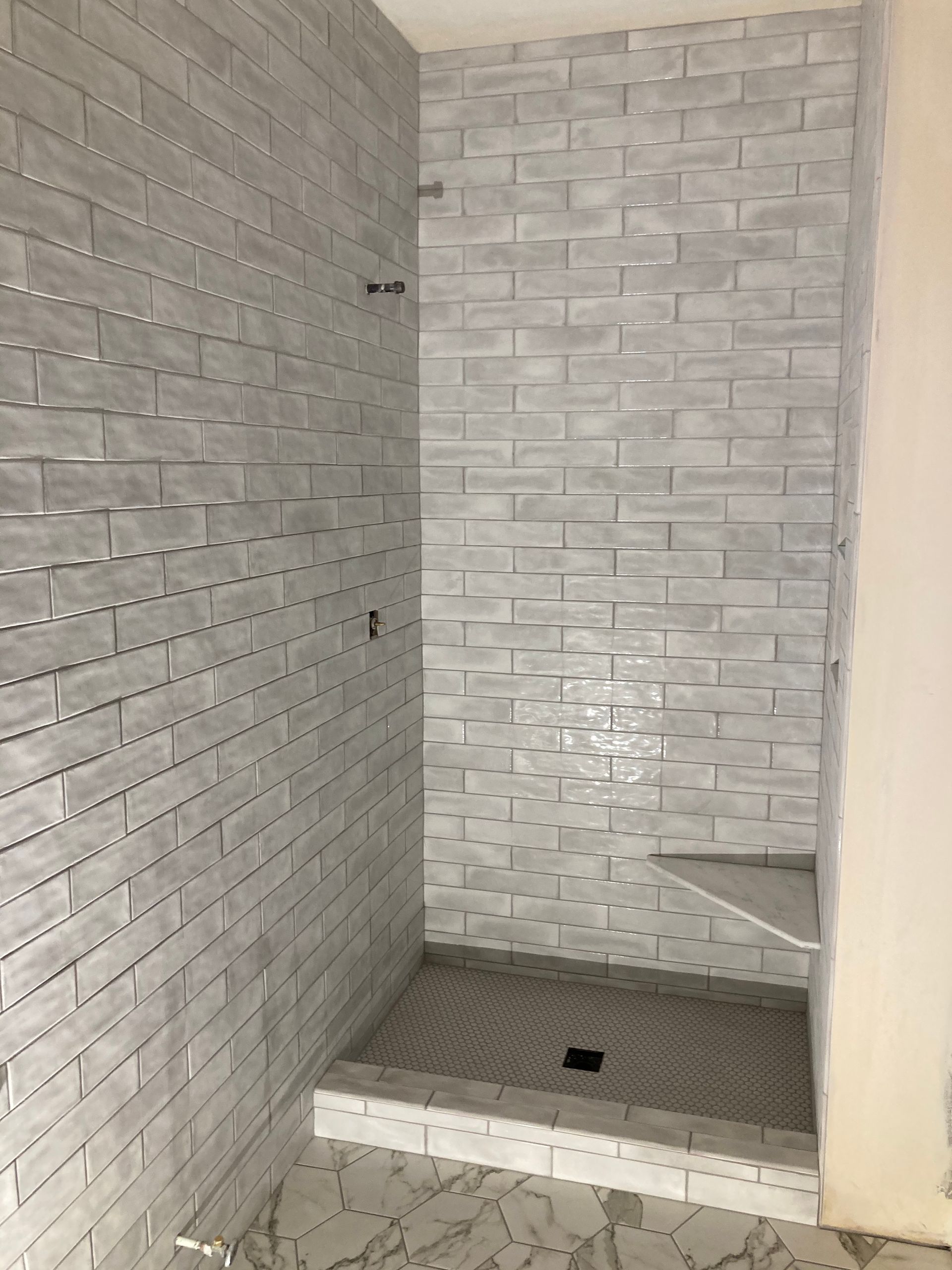 Tiled shower stall with white brick-pattern walls and a small bench.