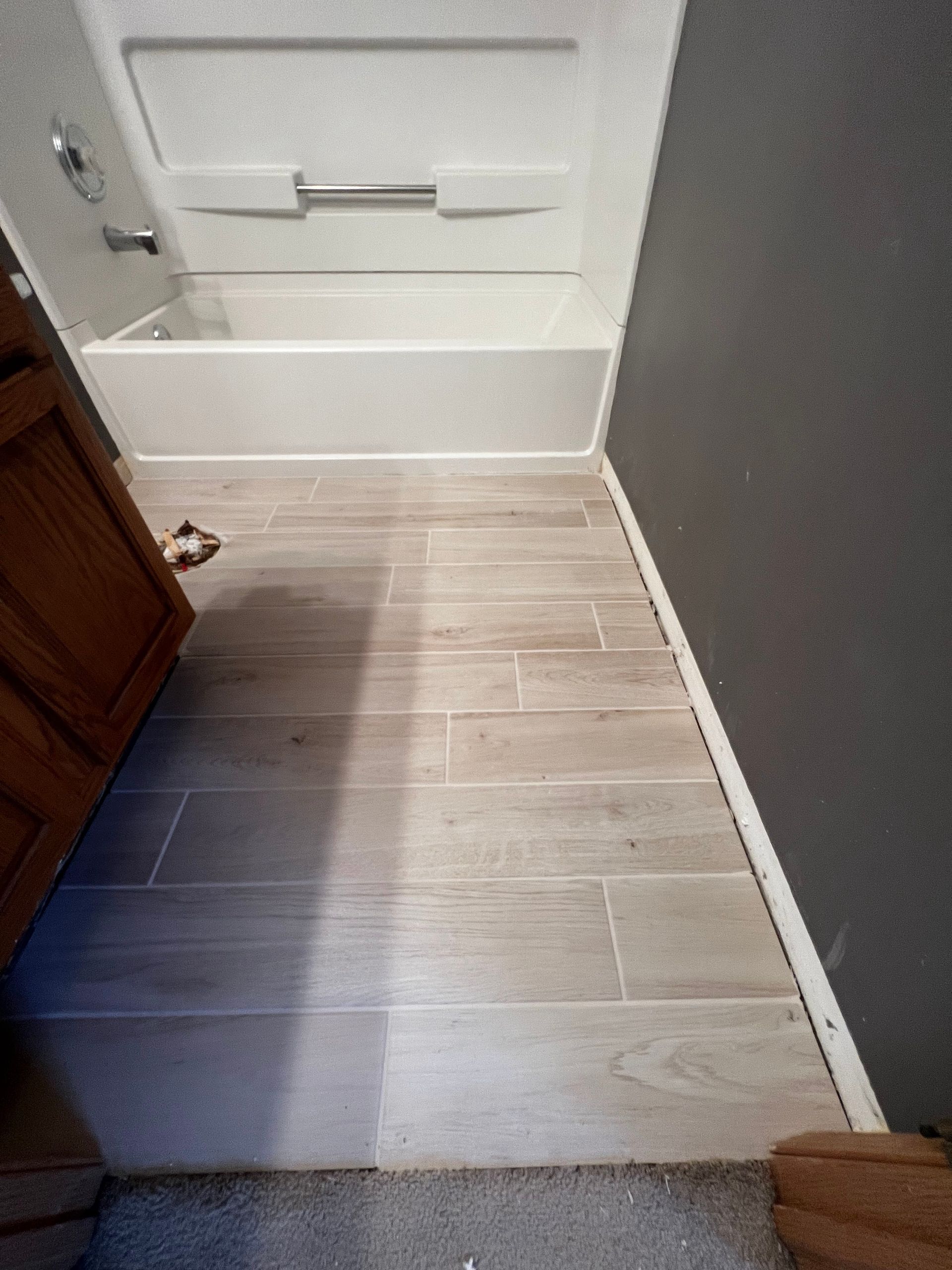 Narrow hallway with beige tile floor, white door, and gray wall; doorway opens into a room.