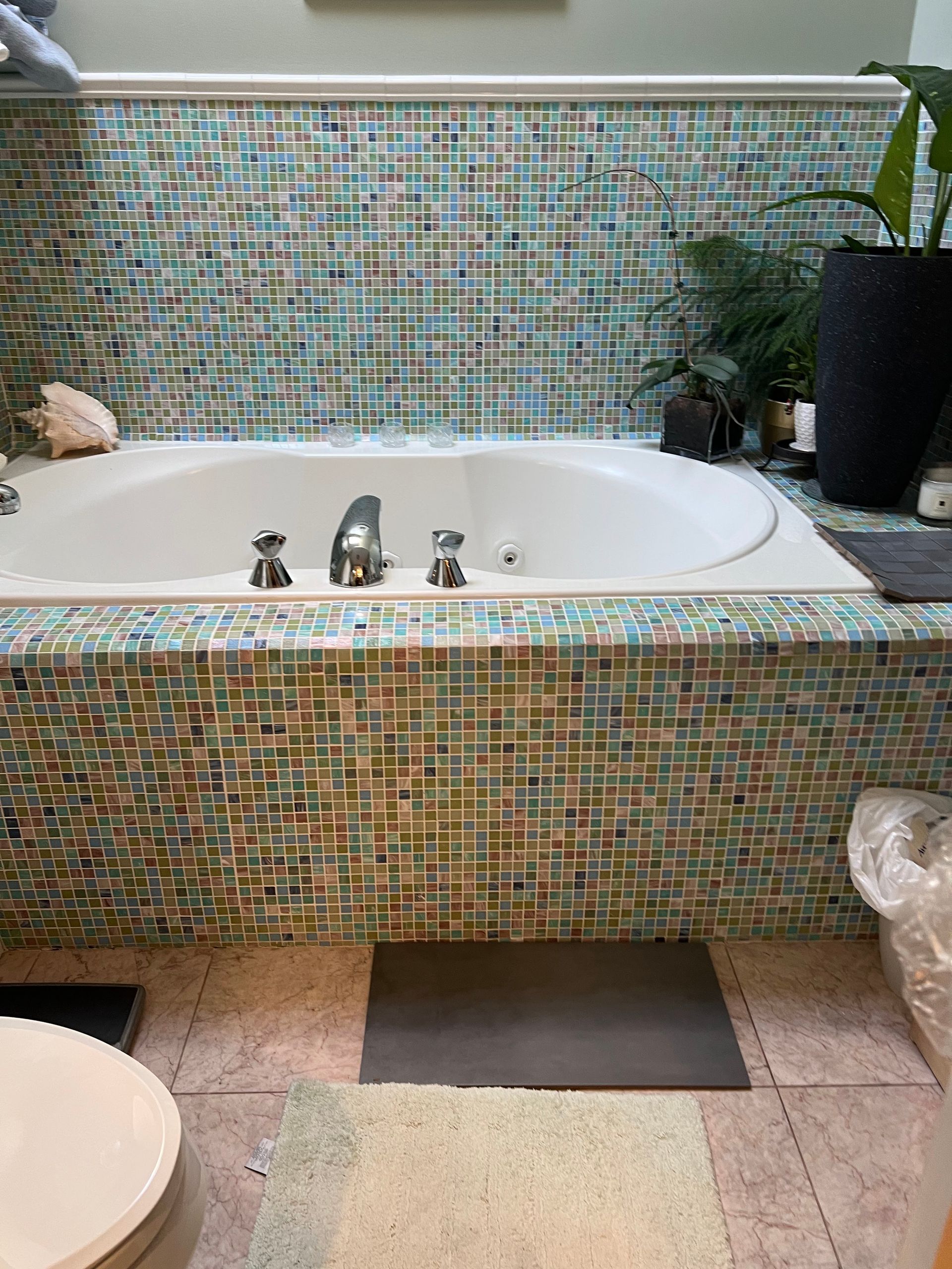 Outdoor mosaic-tiled bathtub with faucet, potted plant, and stone patio floor indoors or in a spa setting