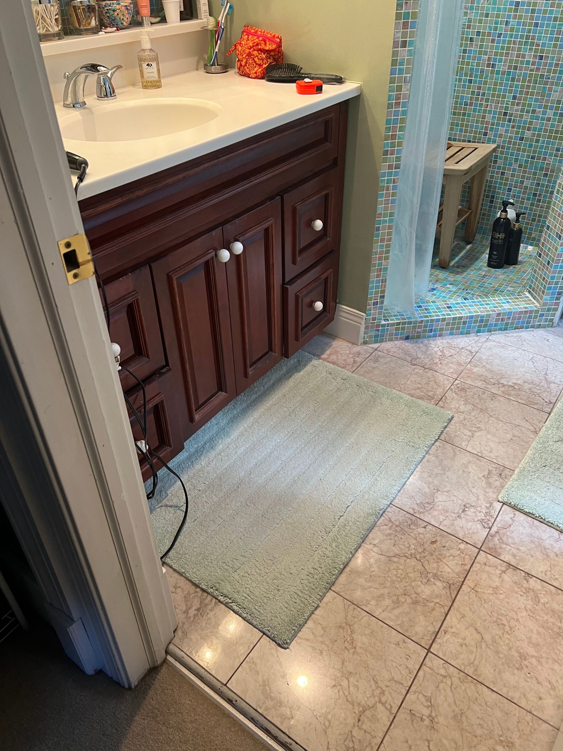 Bathroom sink vanity with dark wood cabinets, white countertop, tiled floor, and glass shower door.