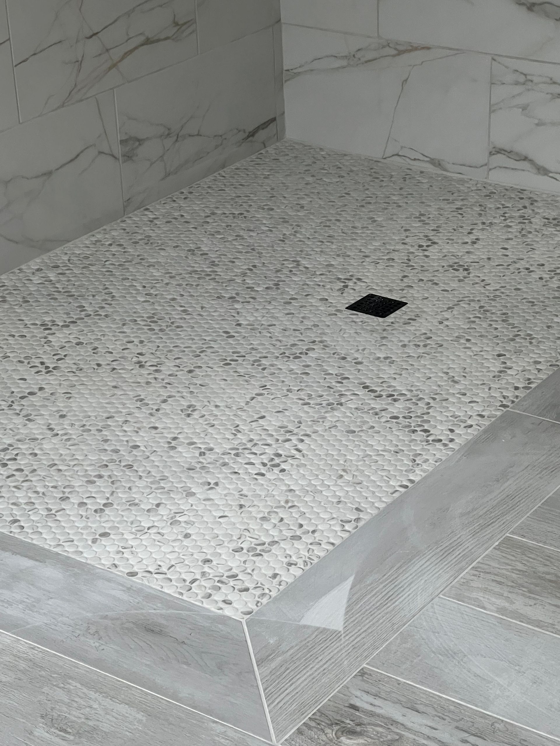 Tiled shower floor with a small black drain opening in the center.