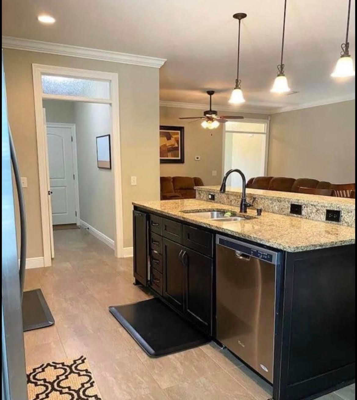 Bright kitchen with granite island, dark cabinets, stainless dishwasher, and pendant lights; dining area beyond.