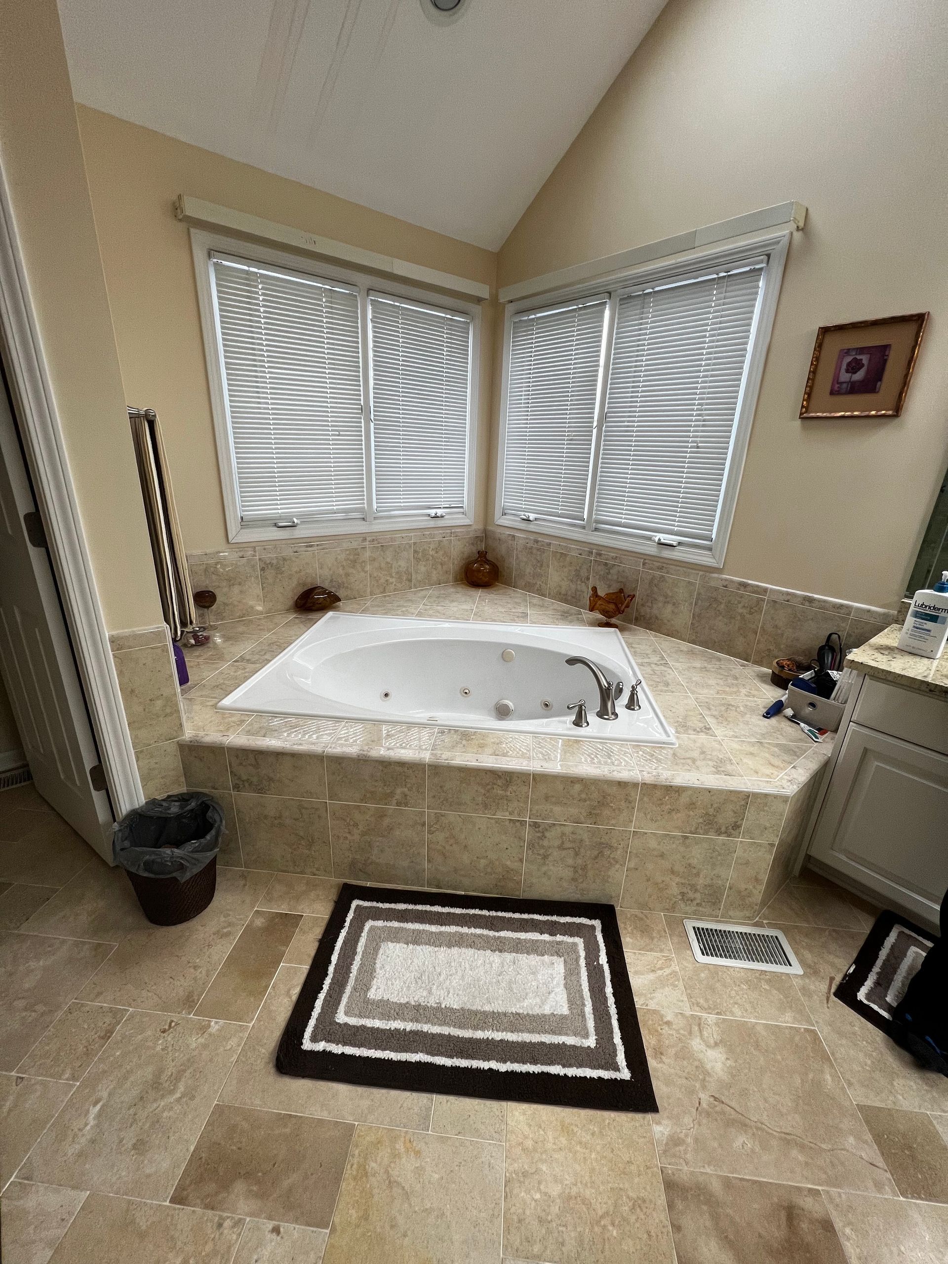 Luxury bathroom with corner jetted tub, beige marble, and striped window blinds