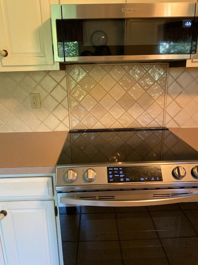 Modern kitchen stove with black cooktop, stainless microwave, and white cabinets on either side
