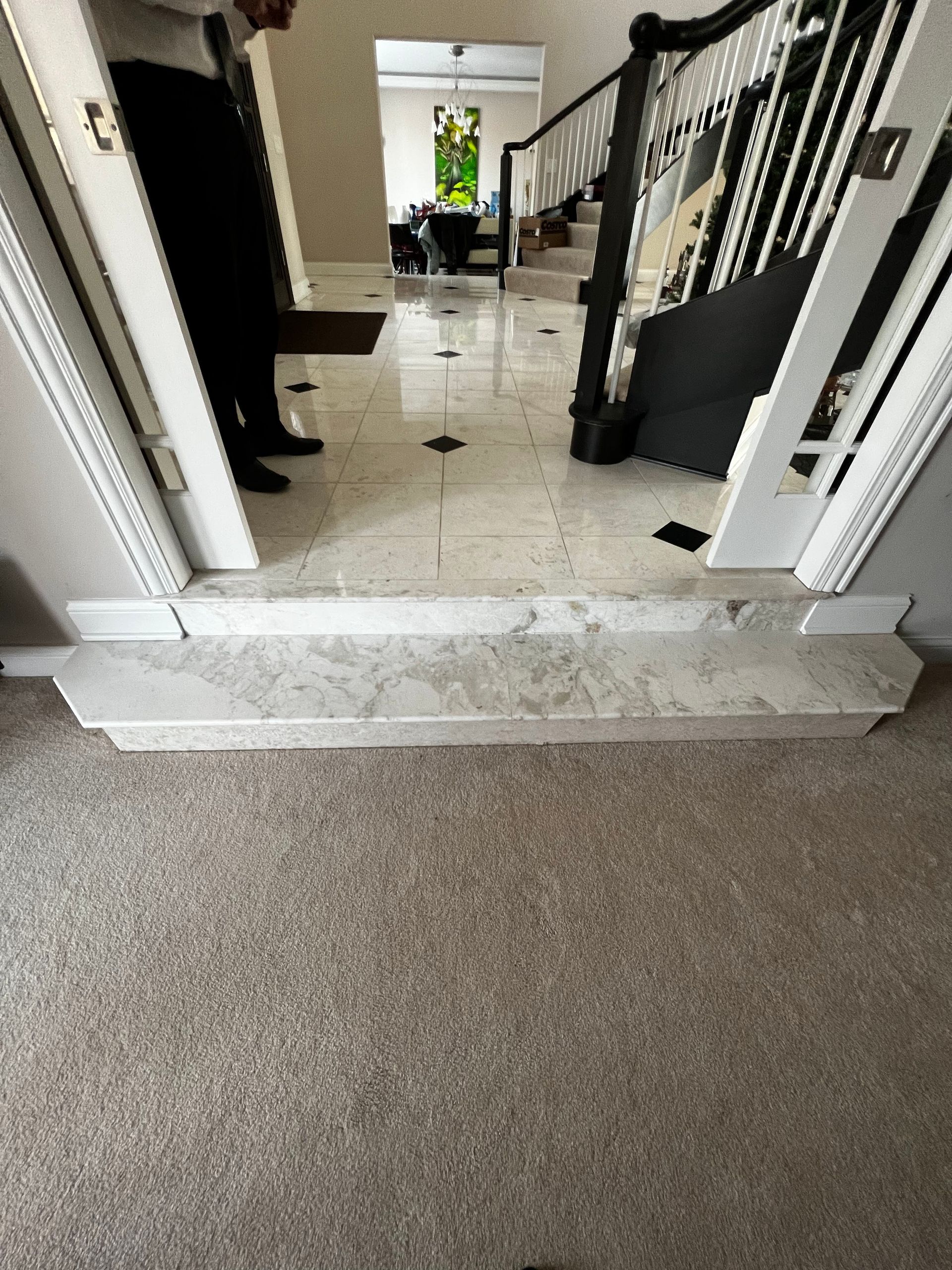 Indoor hallway with tiled floor, carpeted foreground, and open doors leading to a brighter room ahead.