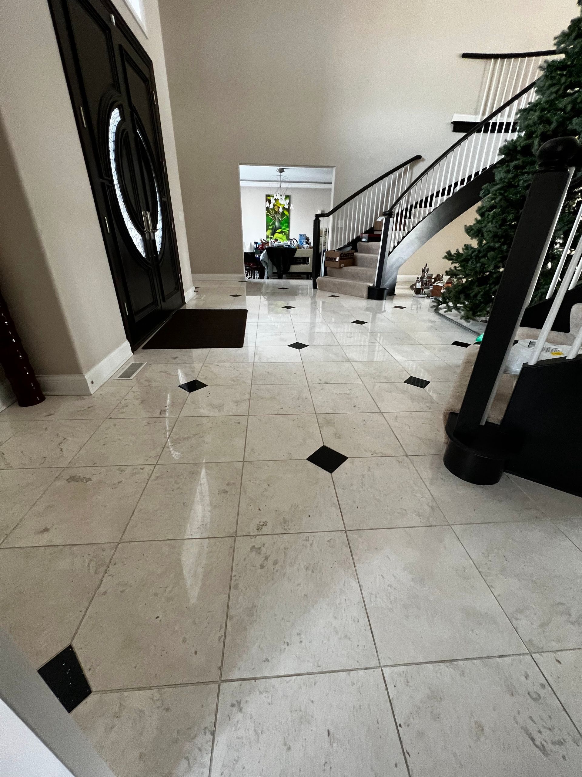 Indoor lobby with glossy tile floor, staircase, and open doorway to a bright exterior.