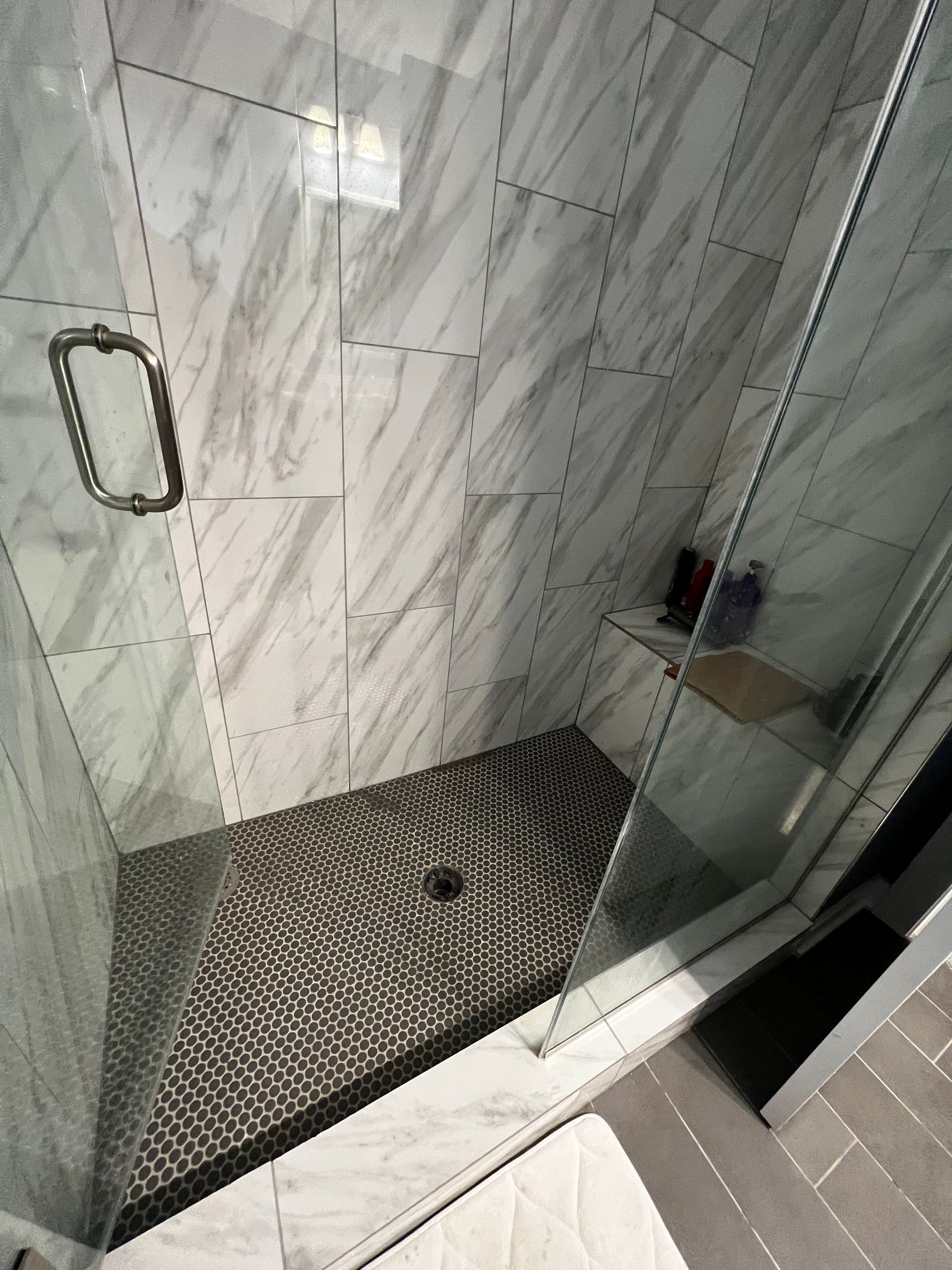 Empty tiled glass shower stall with a mosaic floor and metal handle.