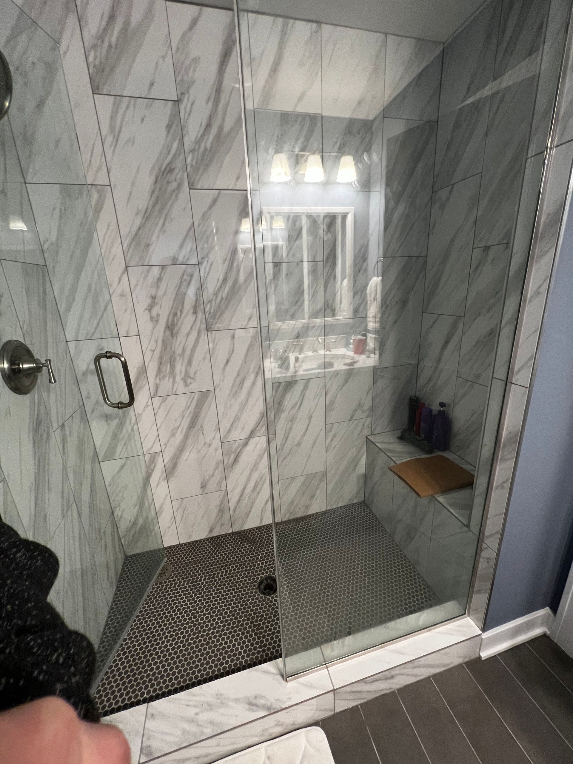 Small walk-in shower with marble-look tile, glass door, and dark hexagon floor tile.