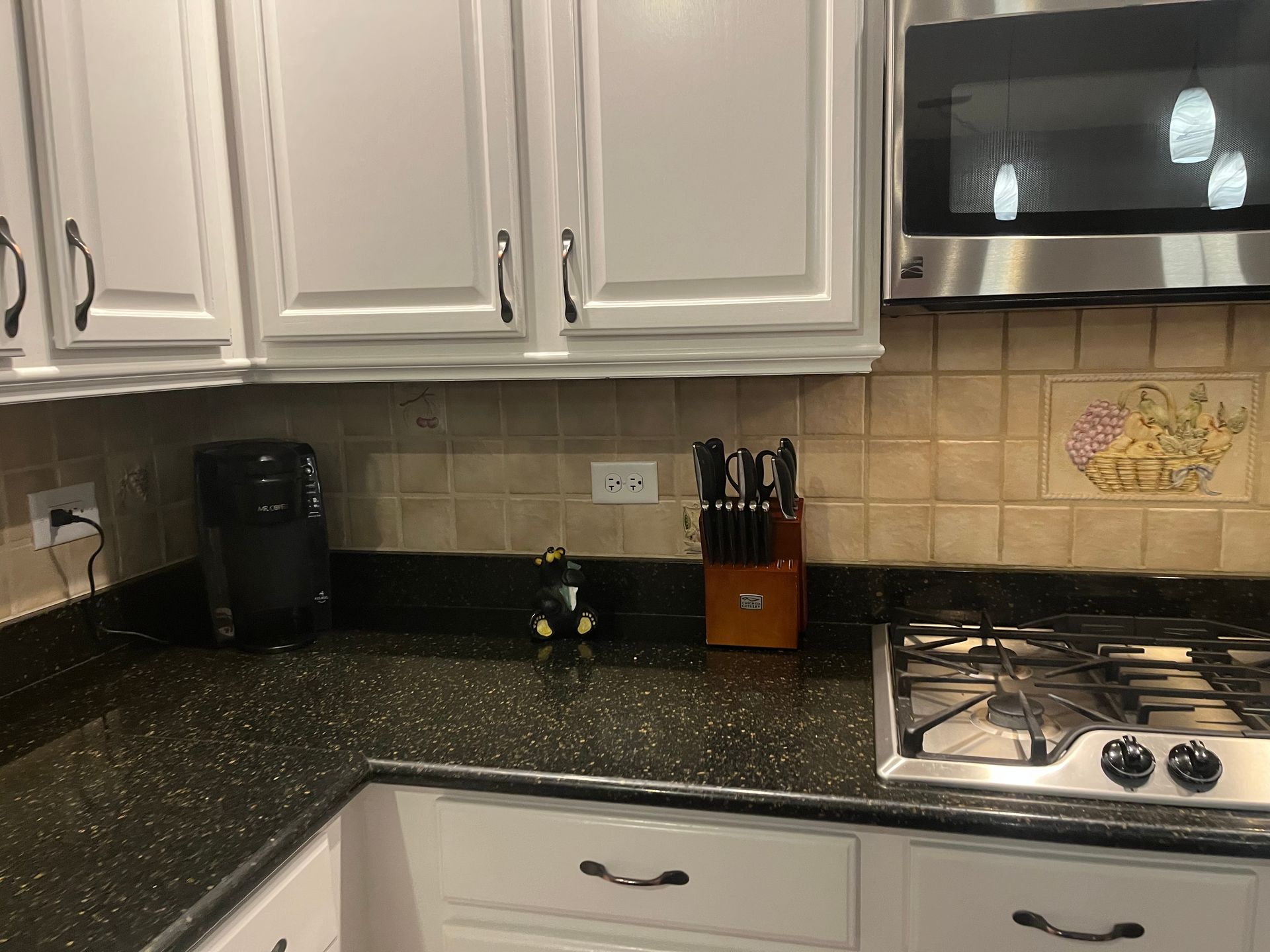 Kitchen countertop with white cabinets, black speckled counters, gas stove, and knife block.