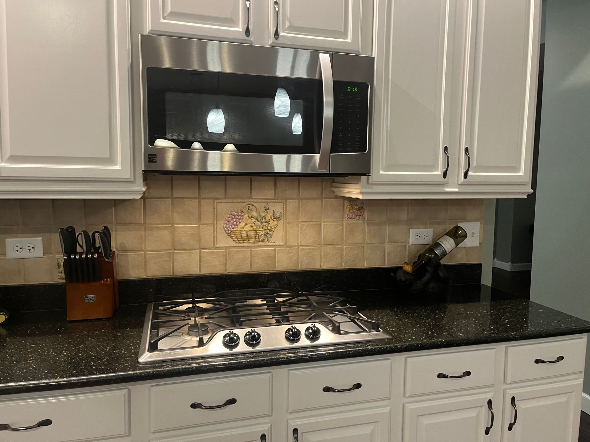 Kitchen stove beneath stainless steel microwave, with tan tile backsplash and granite countertop.
