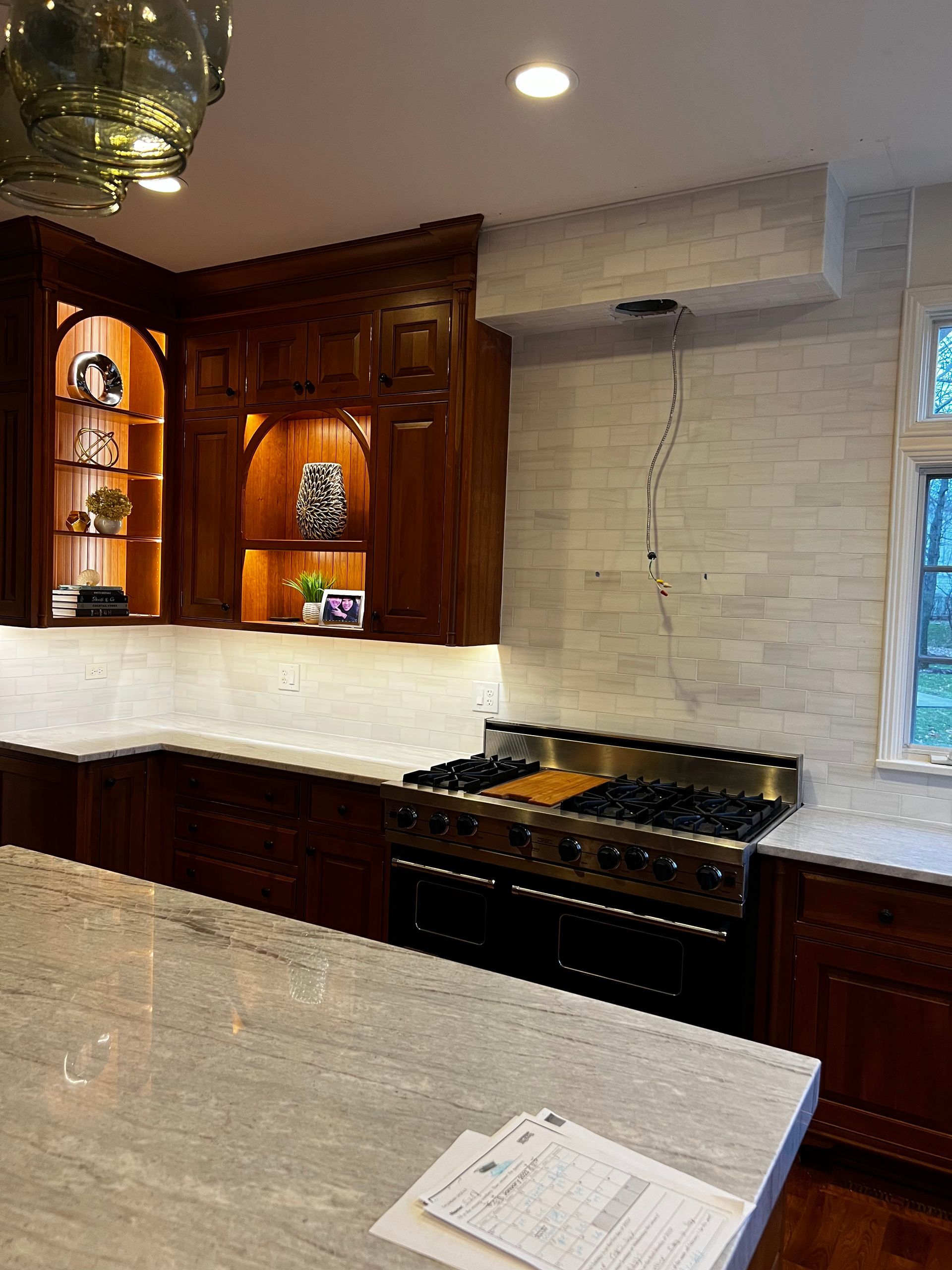 Kitchen with dark wood cabinets, marble backsplash, and a black range beneath a white countertop island.