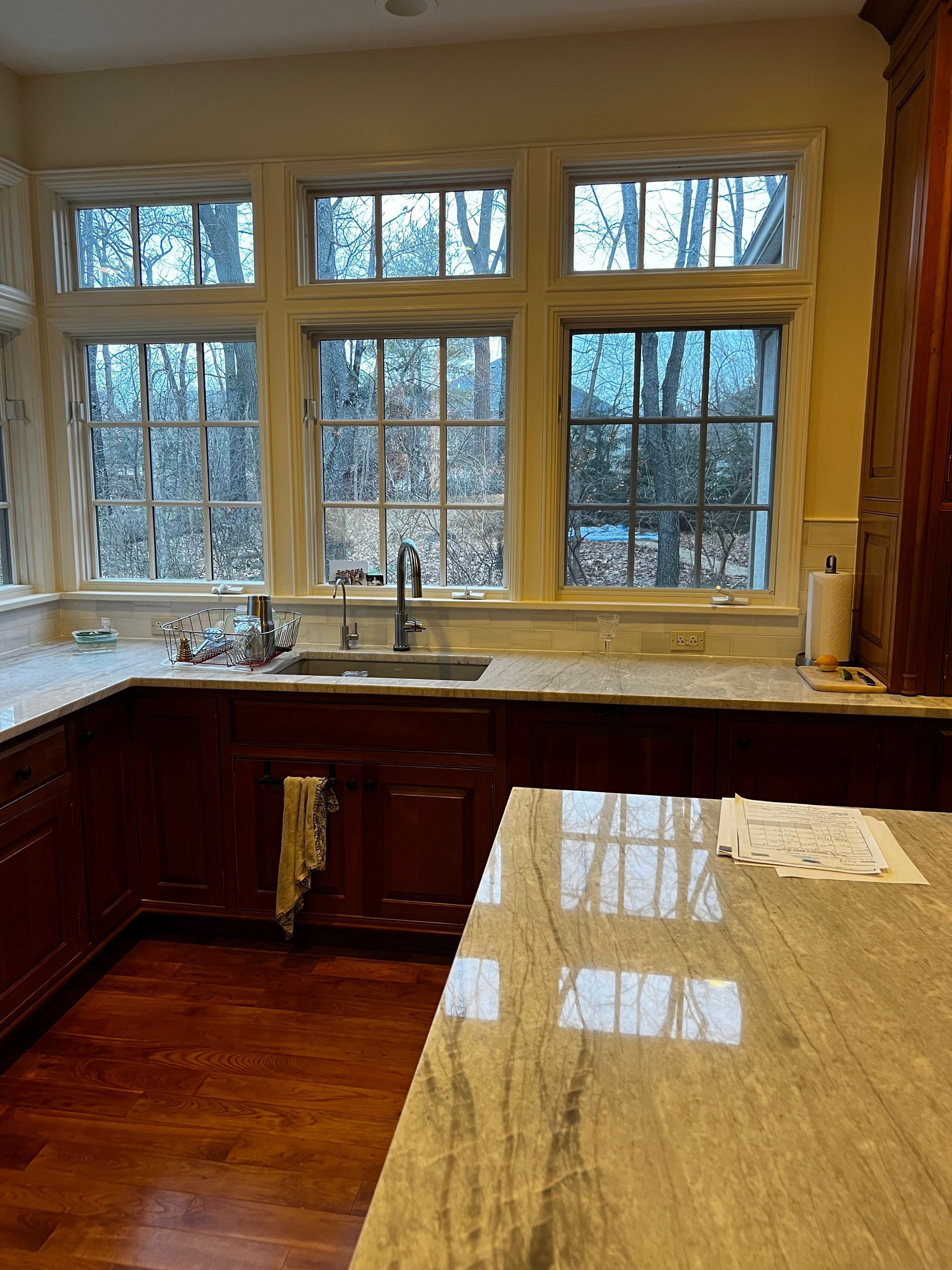 Kitchen with large window, wood cabinets, and hardwood floor reflecting light.
