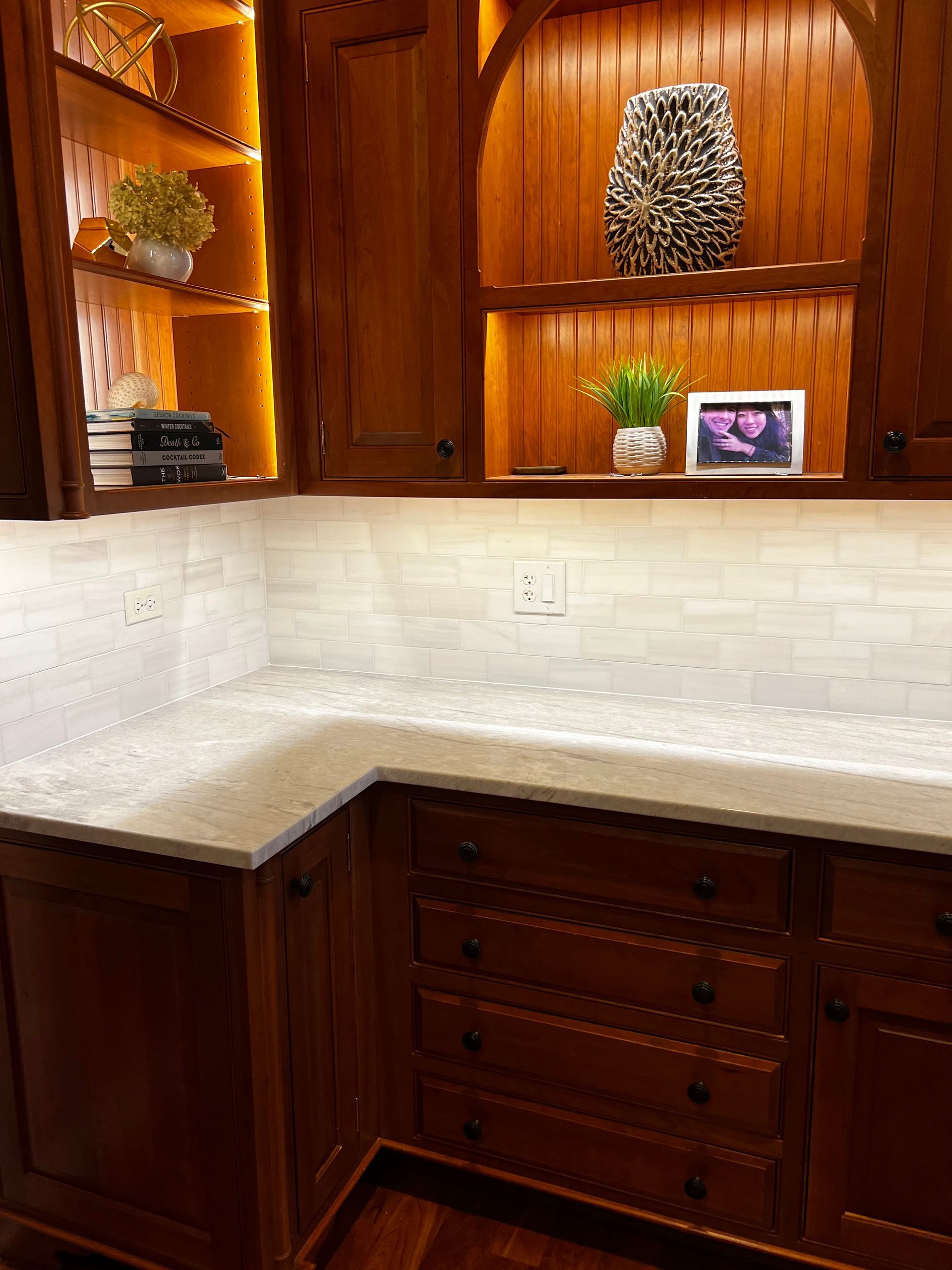Wood-paneled kitchen corner with white countertops, built-in shelves, and under-cabinet lighting