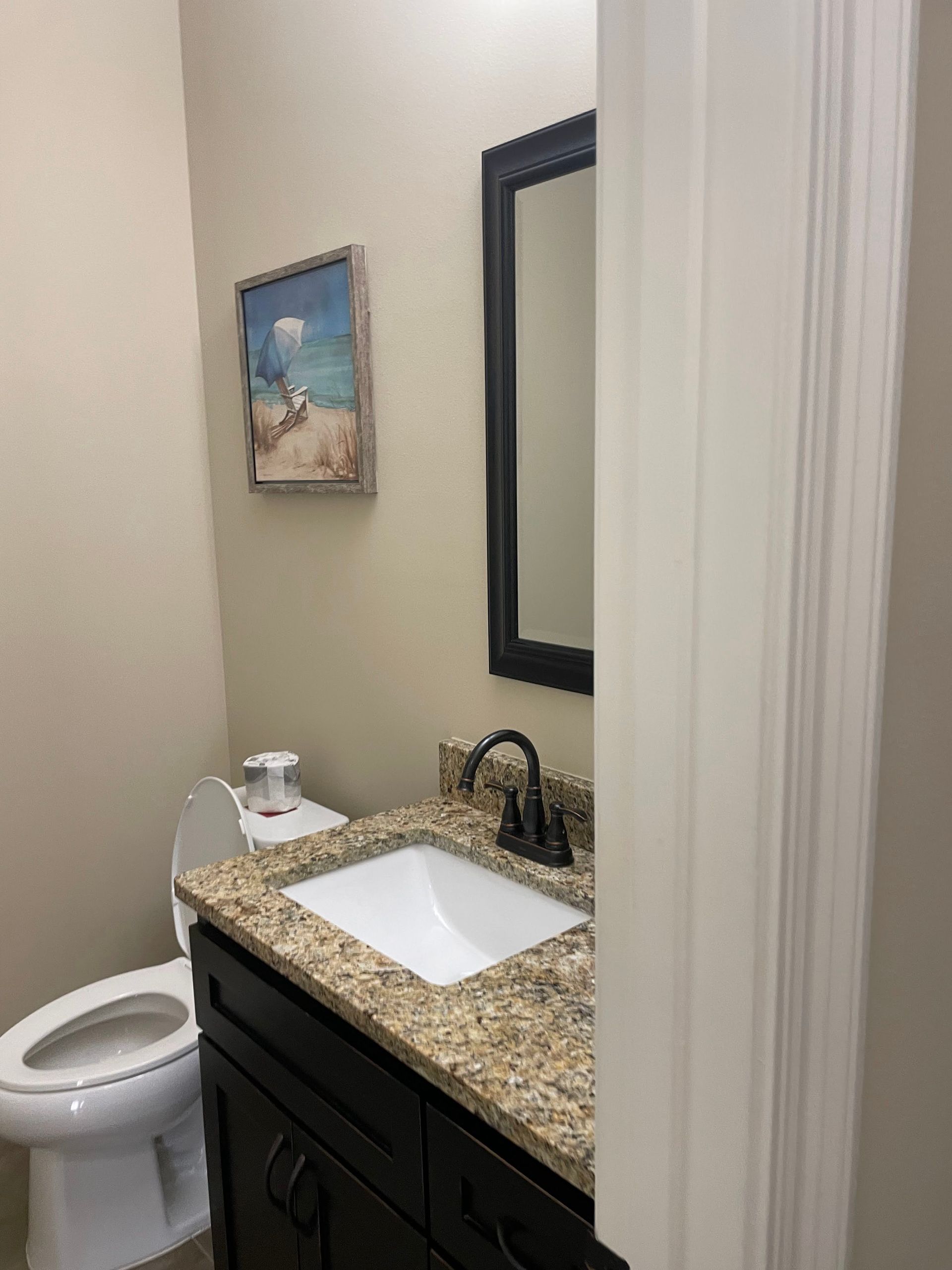 Small bathroom with a toilet, granite sink vanity, and mirror beside a shower curtain.